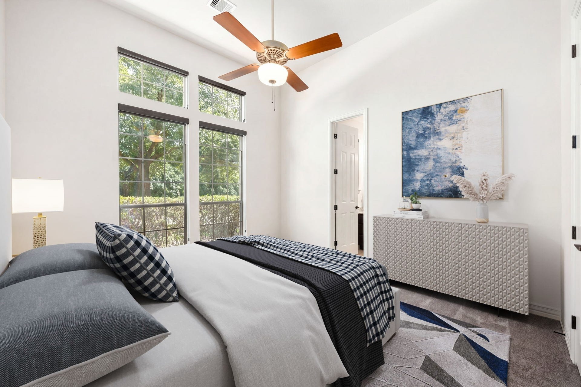 195 Oarwood Place, The Woodlands, TX 77389 Bright secondary bedroom with high ceilings, a ceiling fan, and large windows overlooking the frontyard. The room includes its own private bathroom and a walk-in closet, providing comfort and privacy for family or guests.