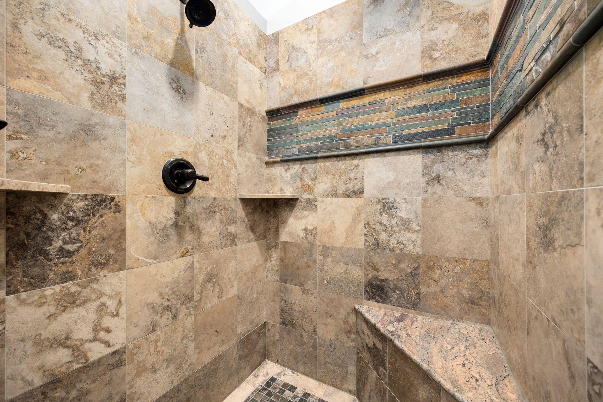 195 Oarwood Place, The Woodlands, TX 77389 Spacious walk-in shower with beautiful natural stone tile, a built-in bench, and convenient storage niches for everyday comfort.
