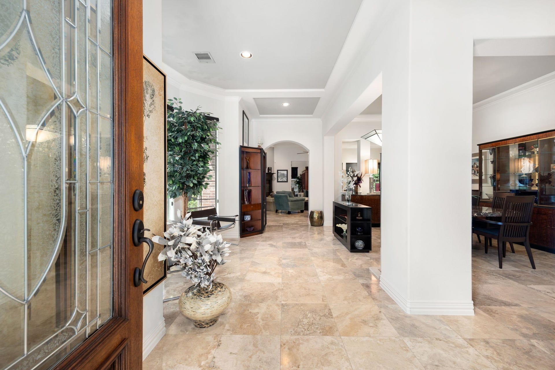 195 Oarwood Place, The Woodlands, TX 77389 Grand foyer with elegant travertine flooring, soaring ceilings, crown molding, and abundant natural light. The impressive entryway creates a warm first impression and flows seamlessly into the formal dining room and main living areas, showcasing the homes open layout and timeless architectural details.