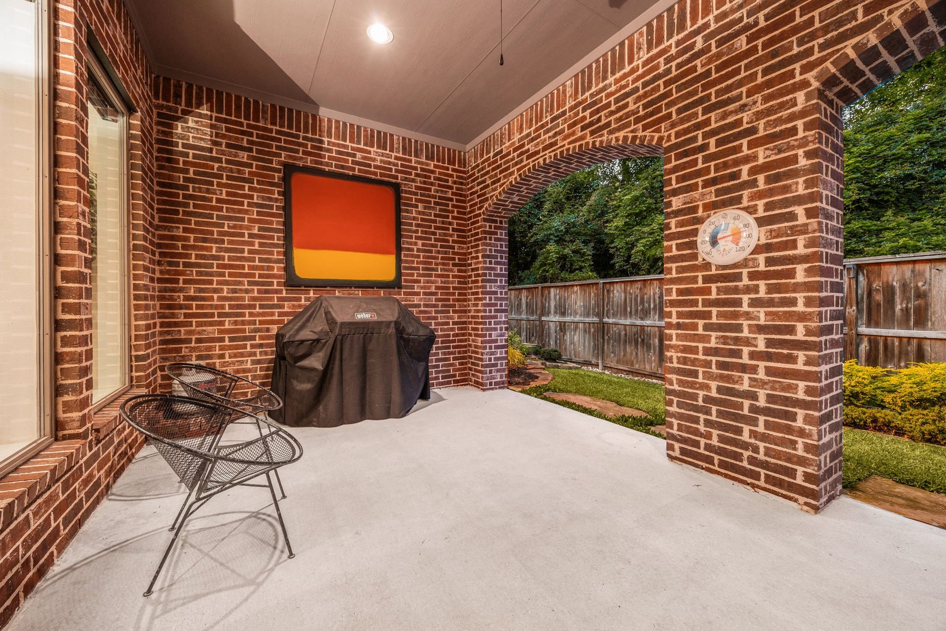 195 Oarwood Place, The Woodlands, TX 77389 This side perspective of the sprawling covered patio reveals a dedicated outdoor culinary and grilling station. Framed by timeless full-brick architecture and majestic arched brick columns, the deep concrete pavilion features recessed evening lighting and opens up to views of the fully fenced, manicured backyard landscape.