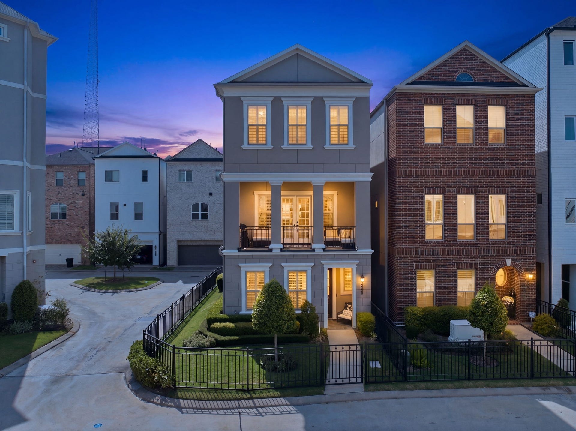 Twilight view of this elegant three-story corner home with a fenced lawn and inviting balcony.