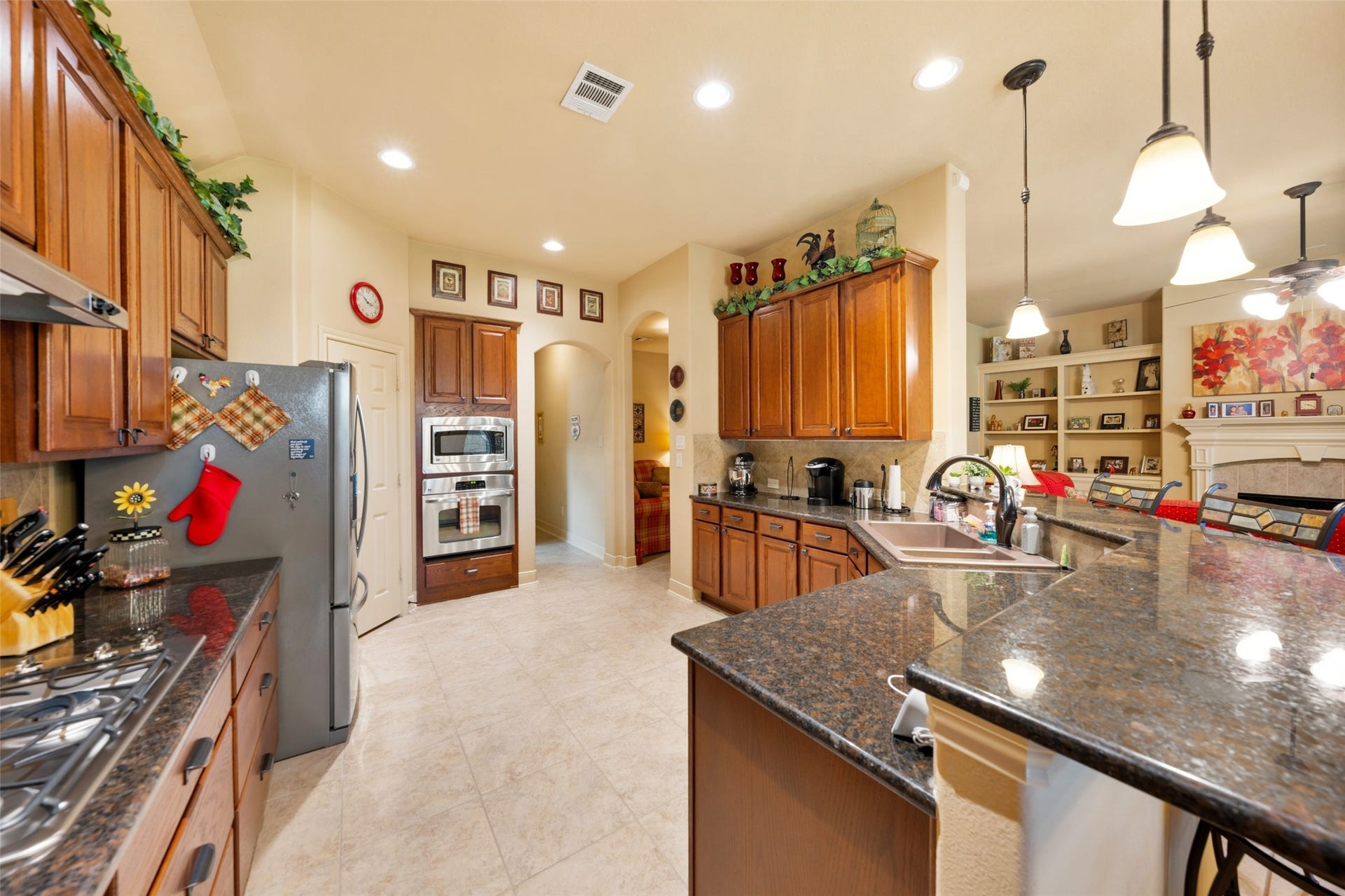 903 Weeping Willow Way, Magnolia, TX 77354 Spacious kitchen with elegant granite countertops, warm wooden cabinetry, stainless steel appliances, and stylish pendant lighting is open to living area and breakfast area.