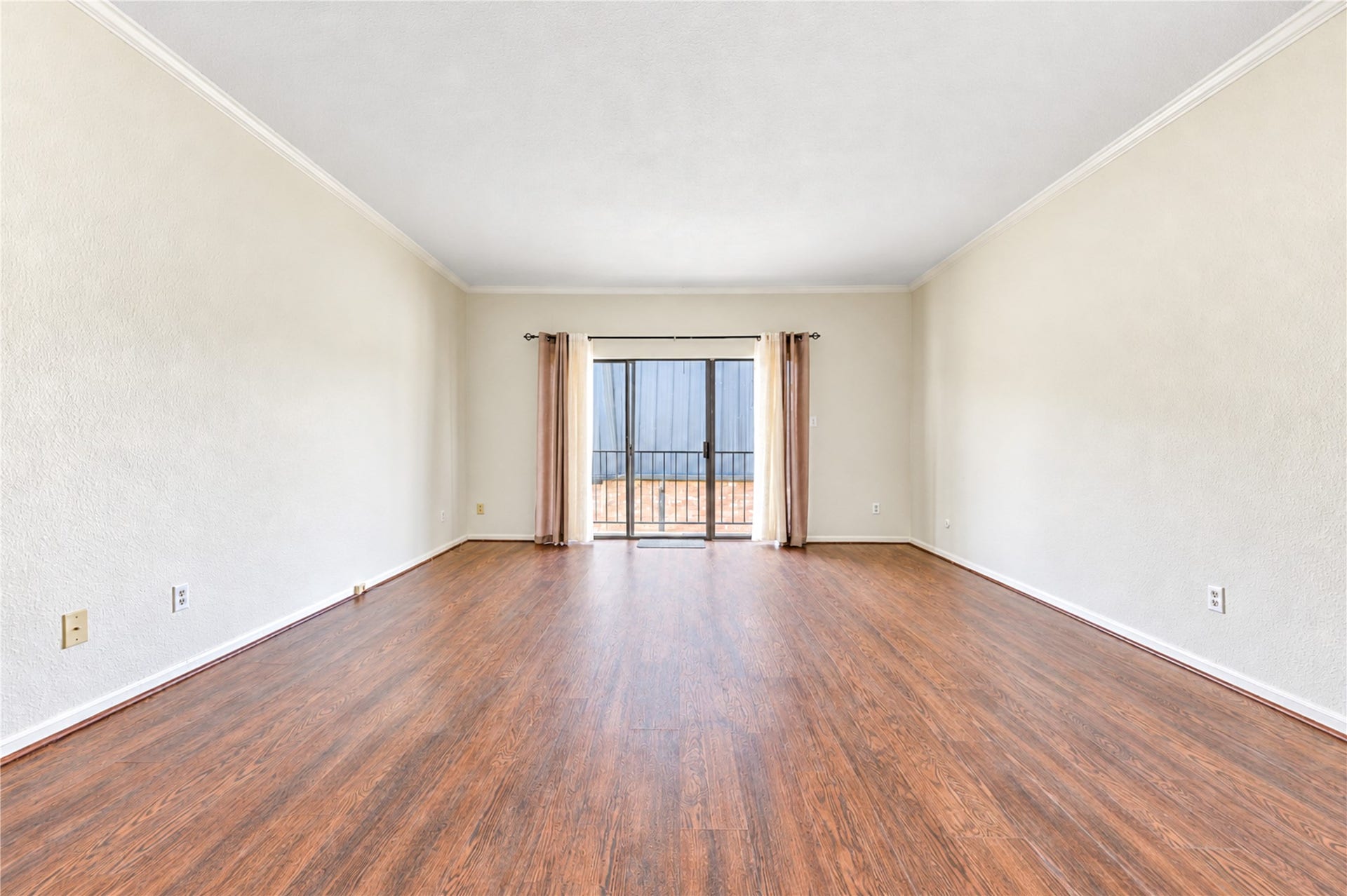 Spacious living area with elegant hardwood flooring and abundant natural light from the sliding glass doors leading to a balcony.