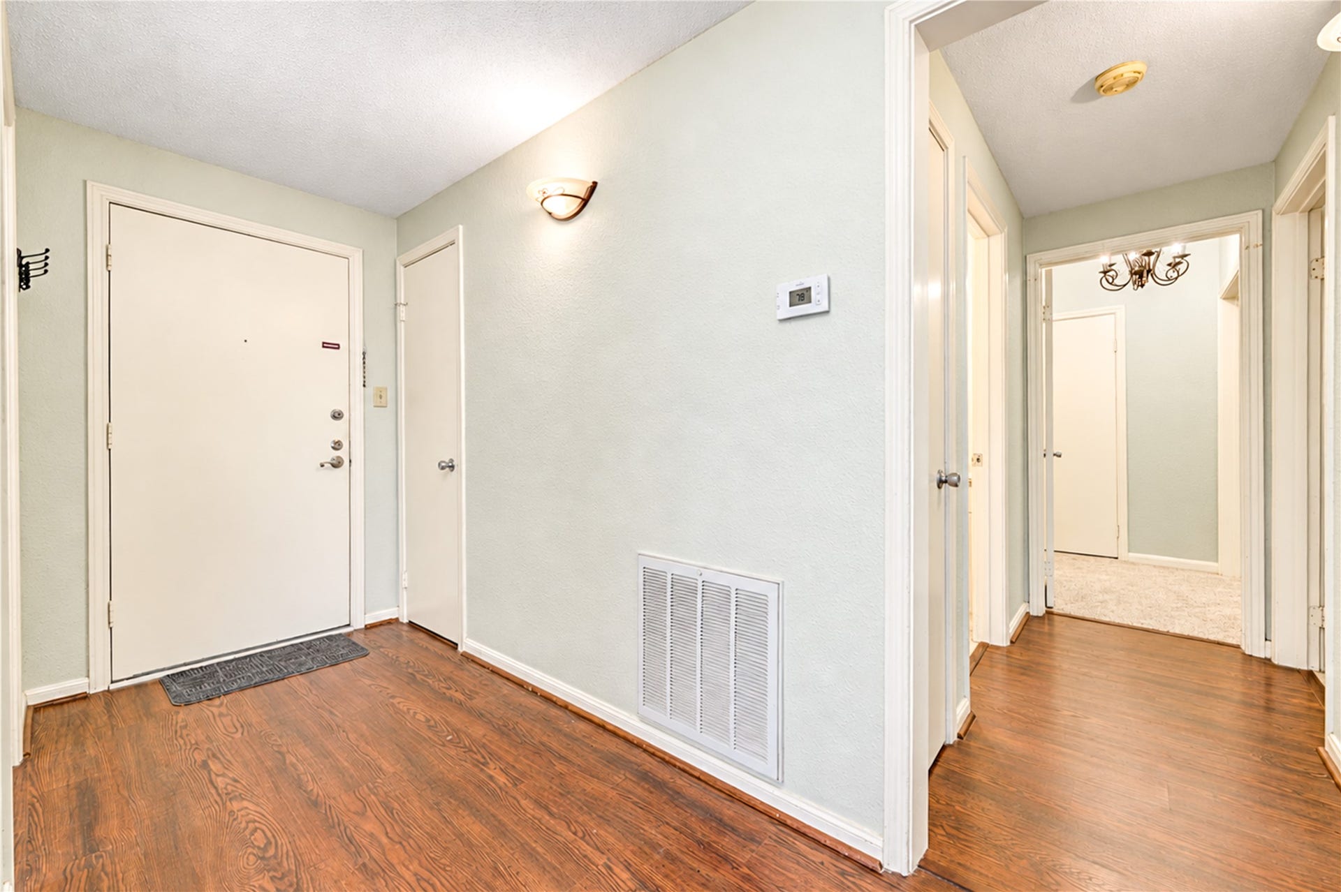 Spacious living area with elegant hardwood flooring, a soft neutral color palette, and a classic chandelier, offering a welcoming ambiance.