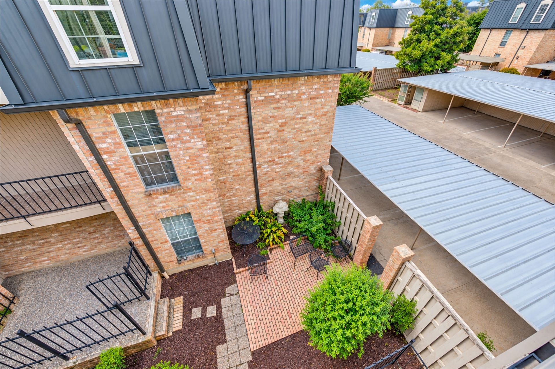 Charming brick townhouse with a modern black mansard roof, offering covered parking and a welcoming entrance in a well-maintained community.