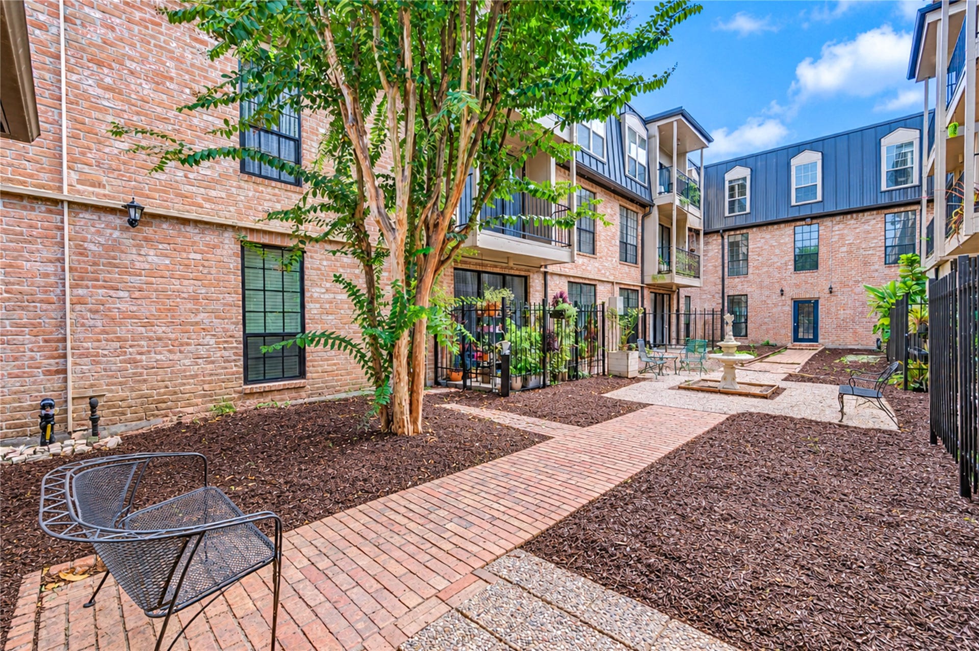 Charming courtyard with a brick walkway, lush greenery, and cozy seating areas, perfect for relaxation and socializing.