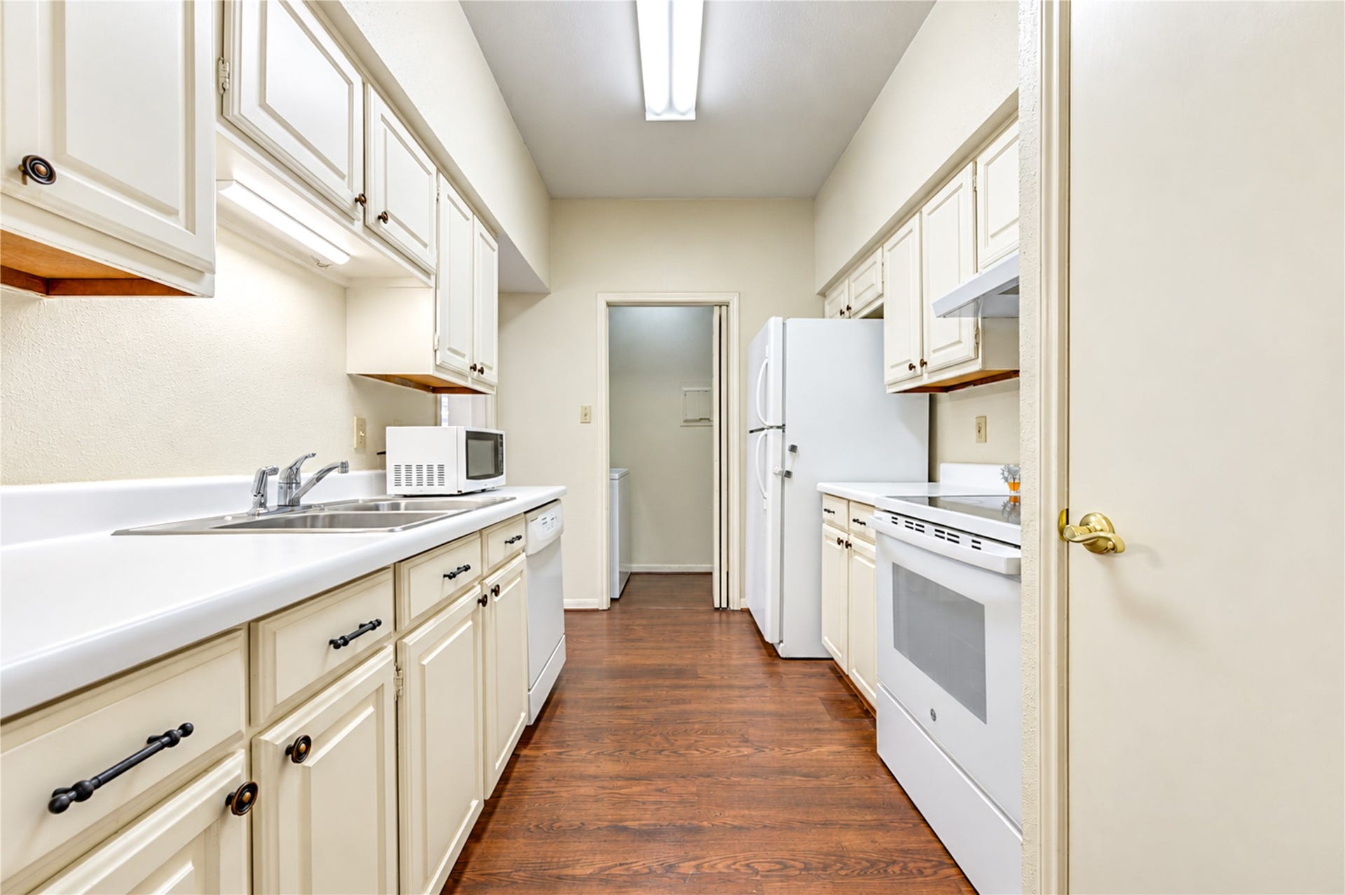 Charming kitchen with classic white cabinetry, sleek appliances, and warm wood flooring, offering a cozy and functional space for culinary endeavors.