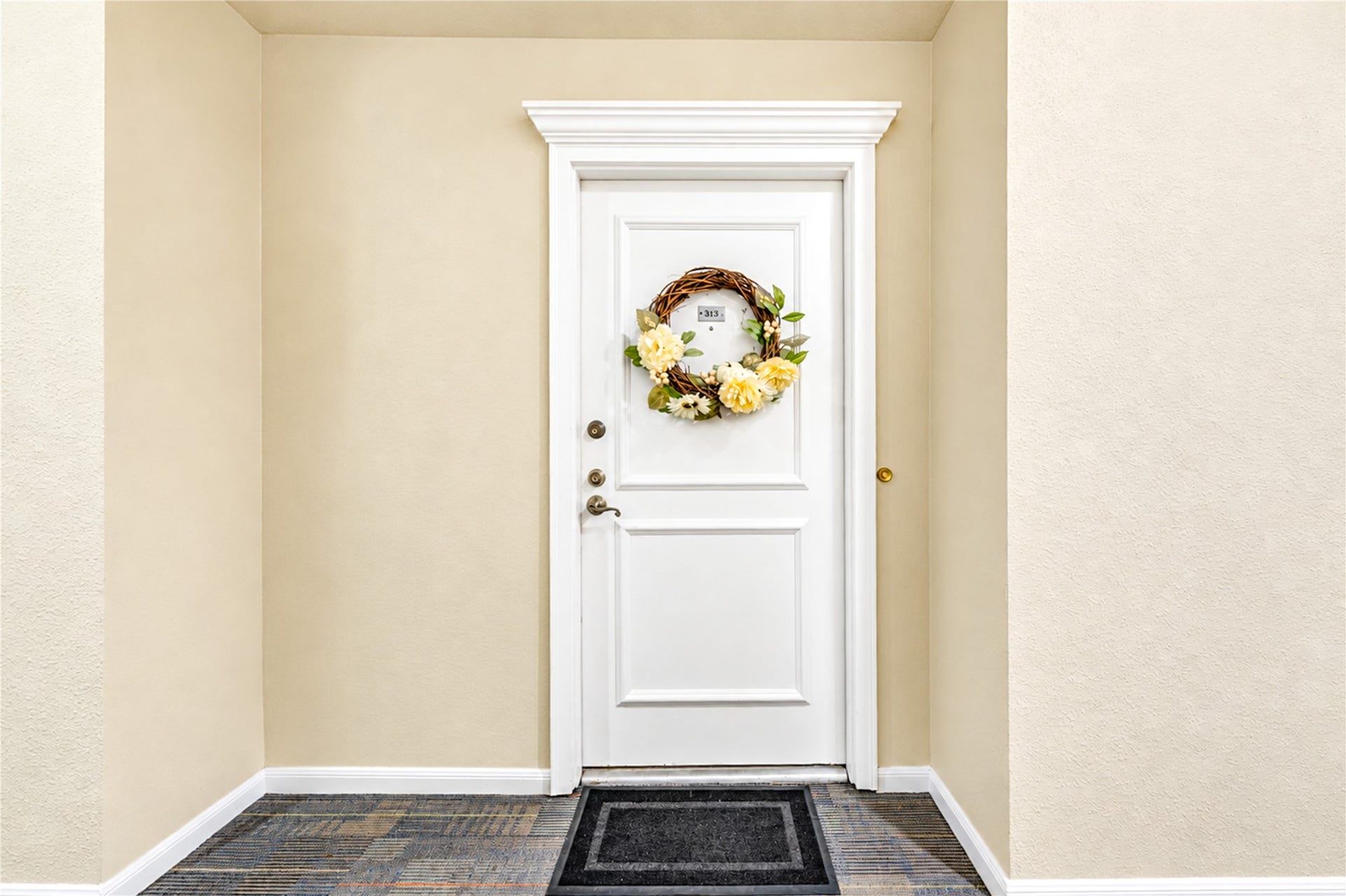 Inviting hallway entrance with a welcoming wreath on the door, featuring modern carpeting and soft lighting for a cozy ambiance.