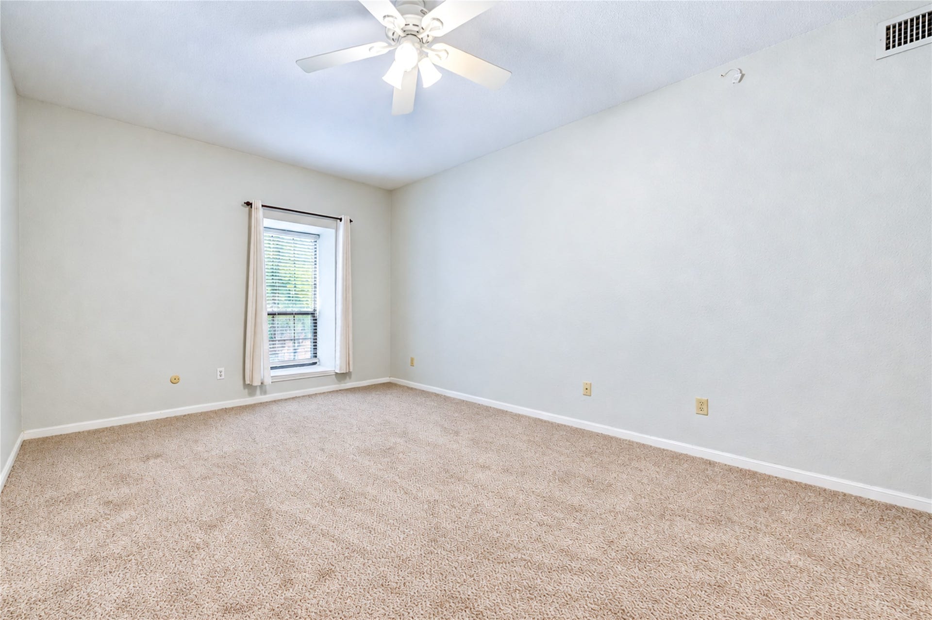 Spacious bedroom featuring soft blue walls, cozy carpeted flooring, and a ceiling fan for comfort, leading to an adjacent bathroom.