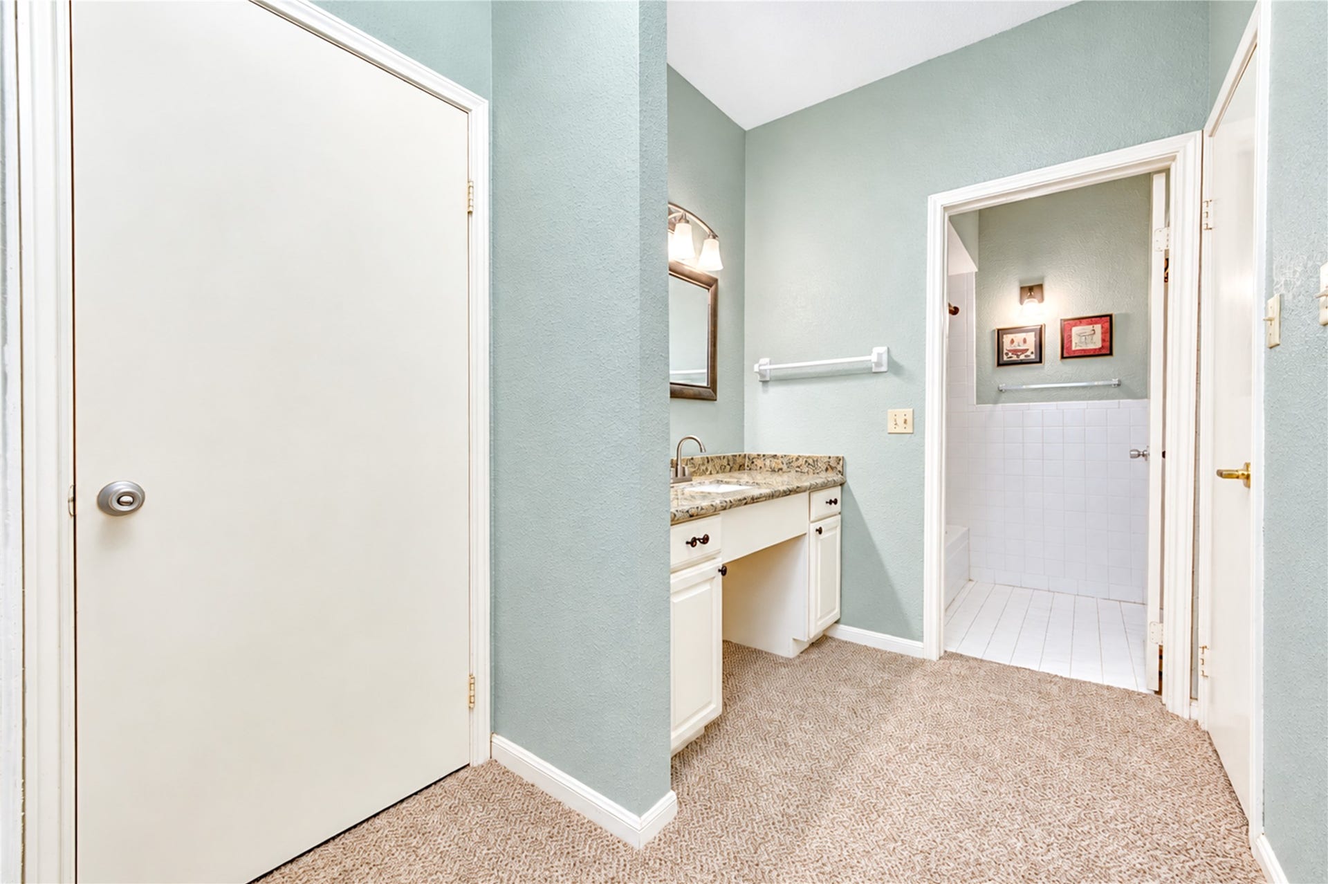 Spacious bathroom with a granite countertop, ample cabinet storage, and soft pastel walls, leading to a tiled shower area.