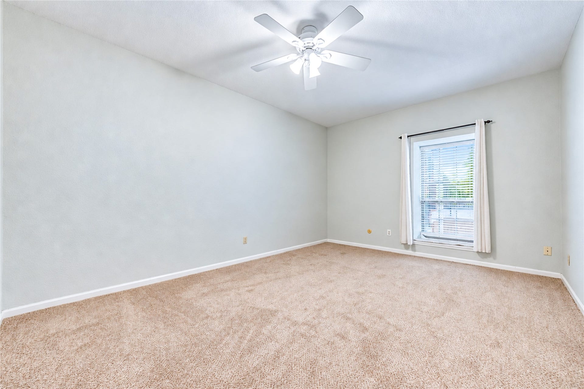Spacious bedroom with plush carpet, natural light from a large window, and a ceiling fan for comfort.