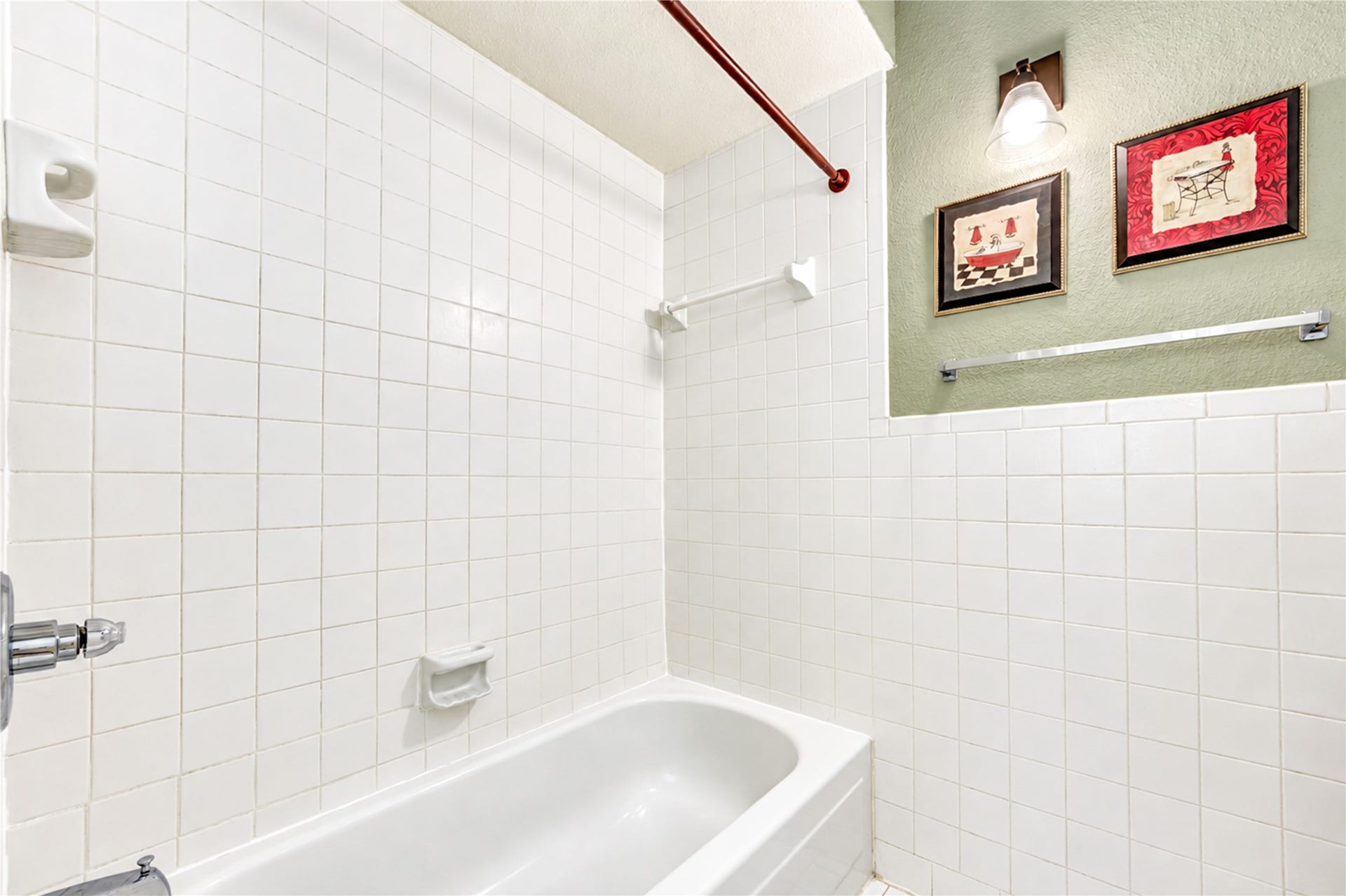 Bright bathroom features a clean white tiled shower-tub combo with convenient built-in shelving, adjacent to a cozy carpeted bedroom with elegant chandelier.