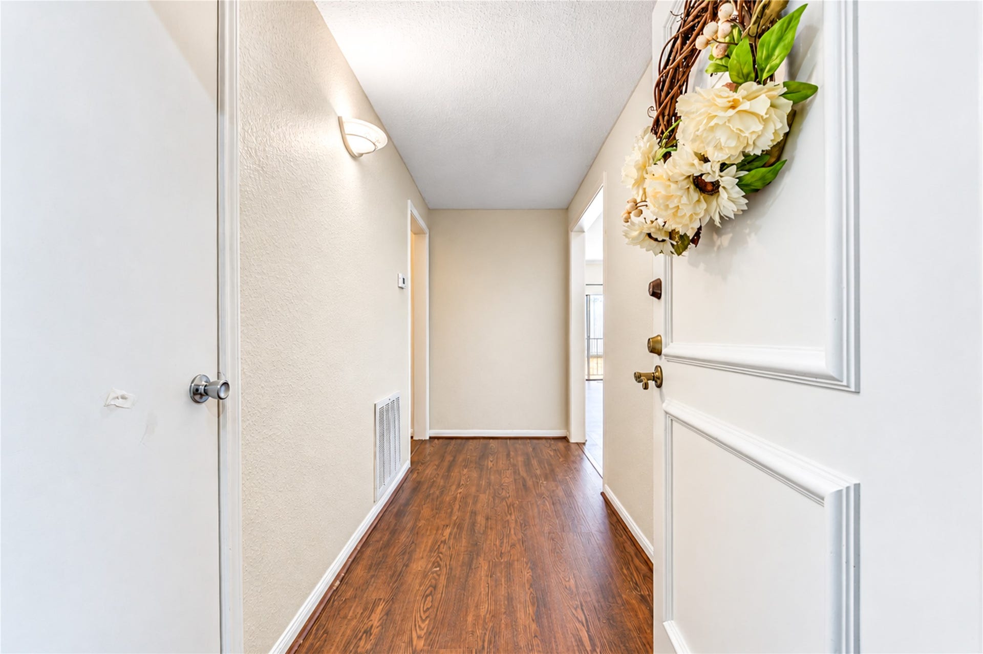 Inviting hallway with soft lighting and a welcoming door adorned with a charming floral wreath, leading to a cozy home.