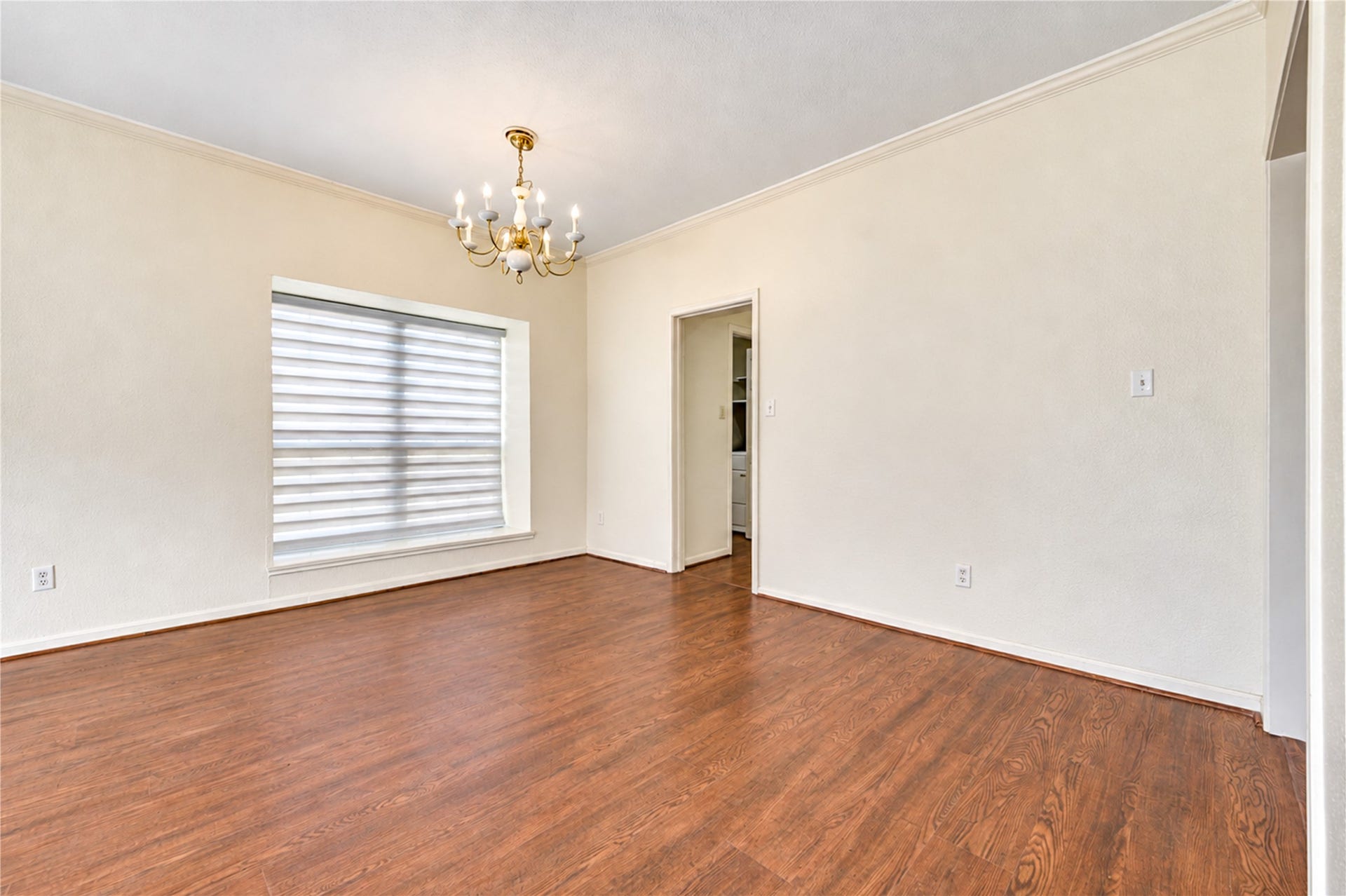 Spacious living area with rich hardwood floors, elegant chandelier, and abundant natural light from large windows and sliding glass doors.