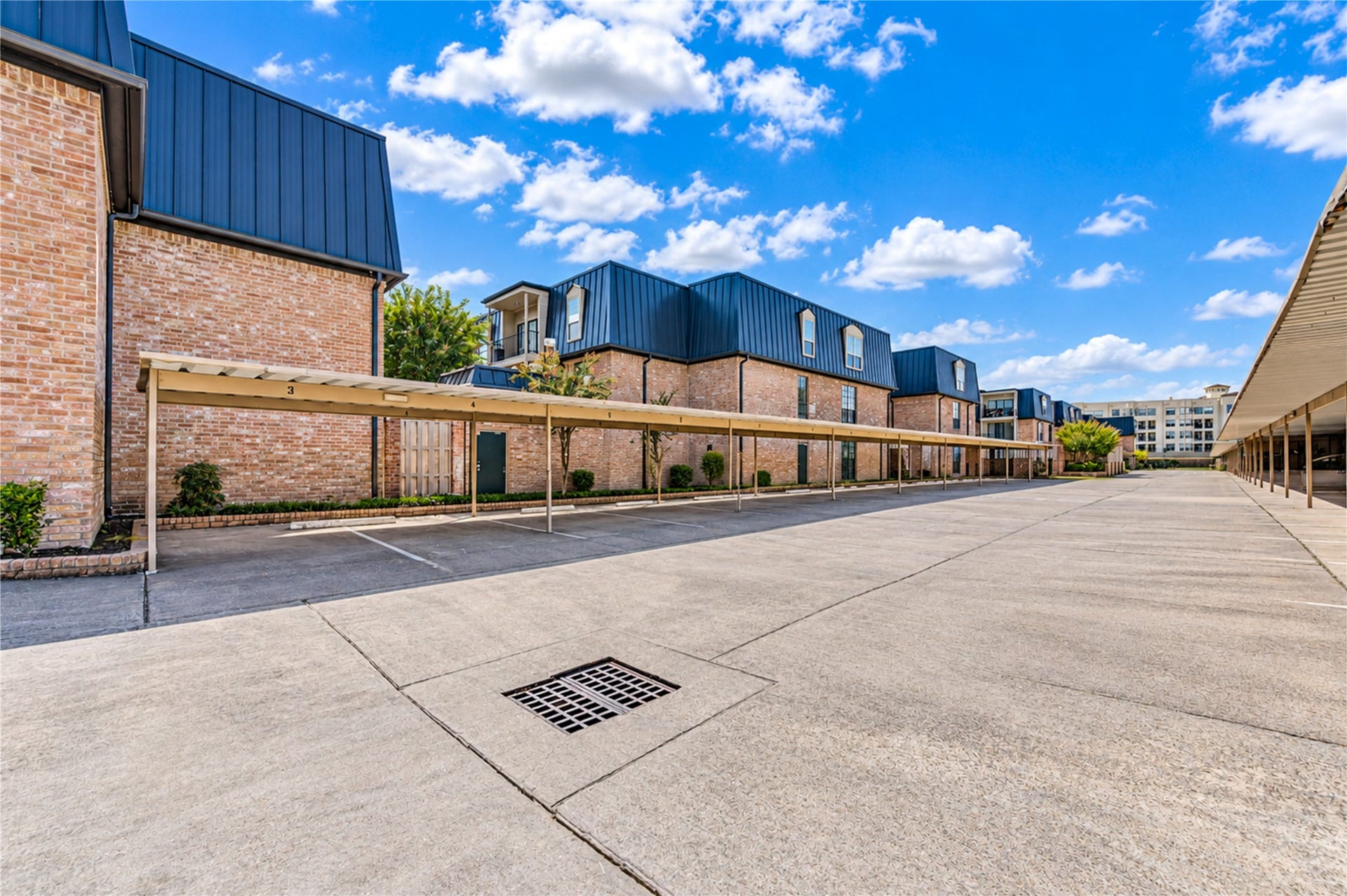 Charming brick townhouse with modern roofing and covered parking, set in a spacious, well-maintained complex with ample parking space and greenery.