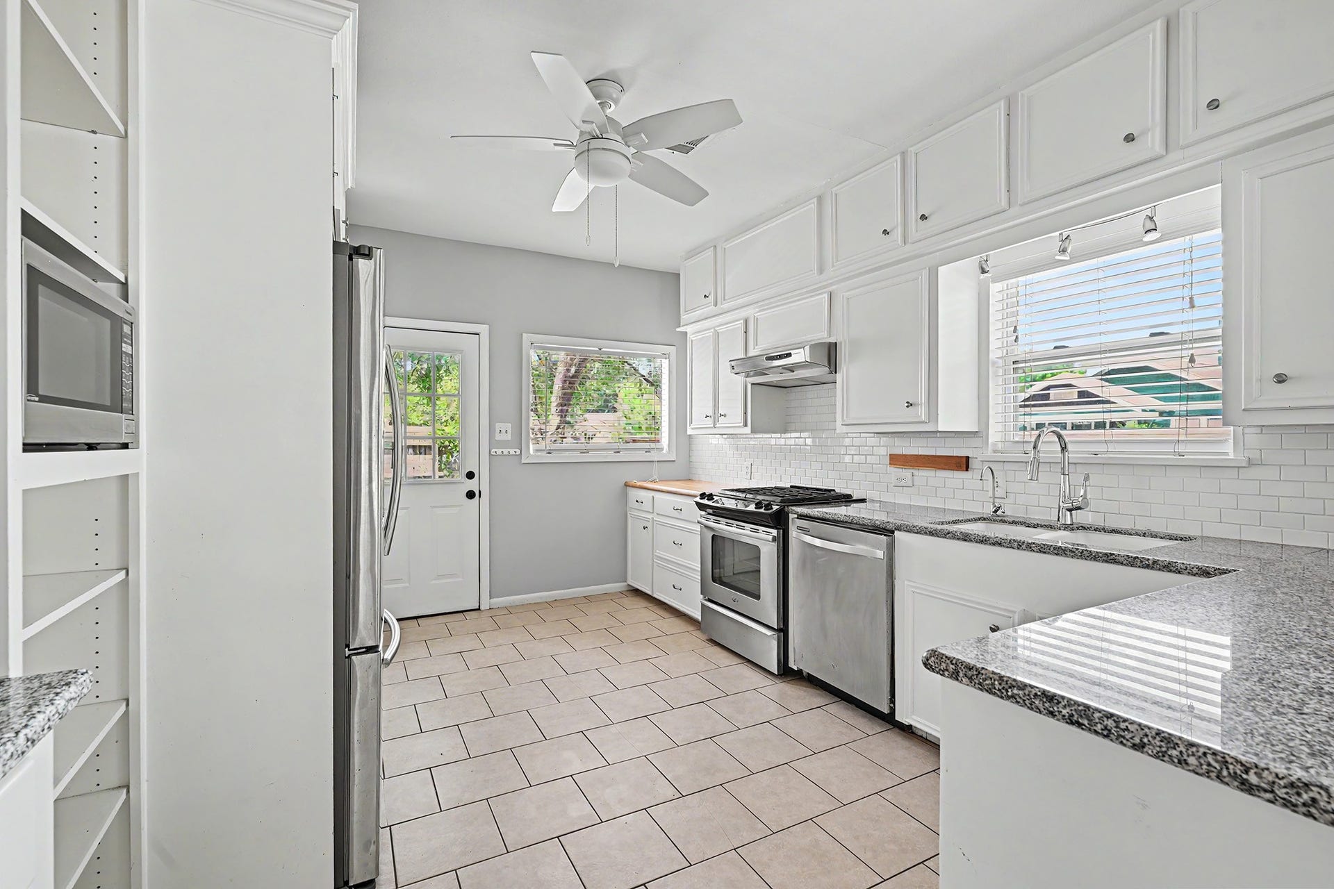 Well-appointed kitchen features granite countertops, classic white subway tile backsplash, gas range, and ample storage.