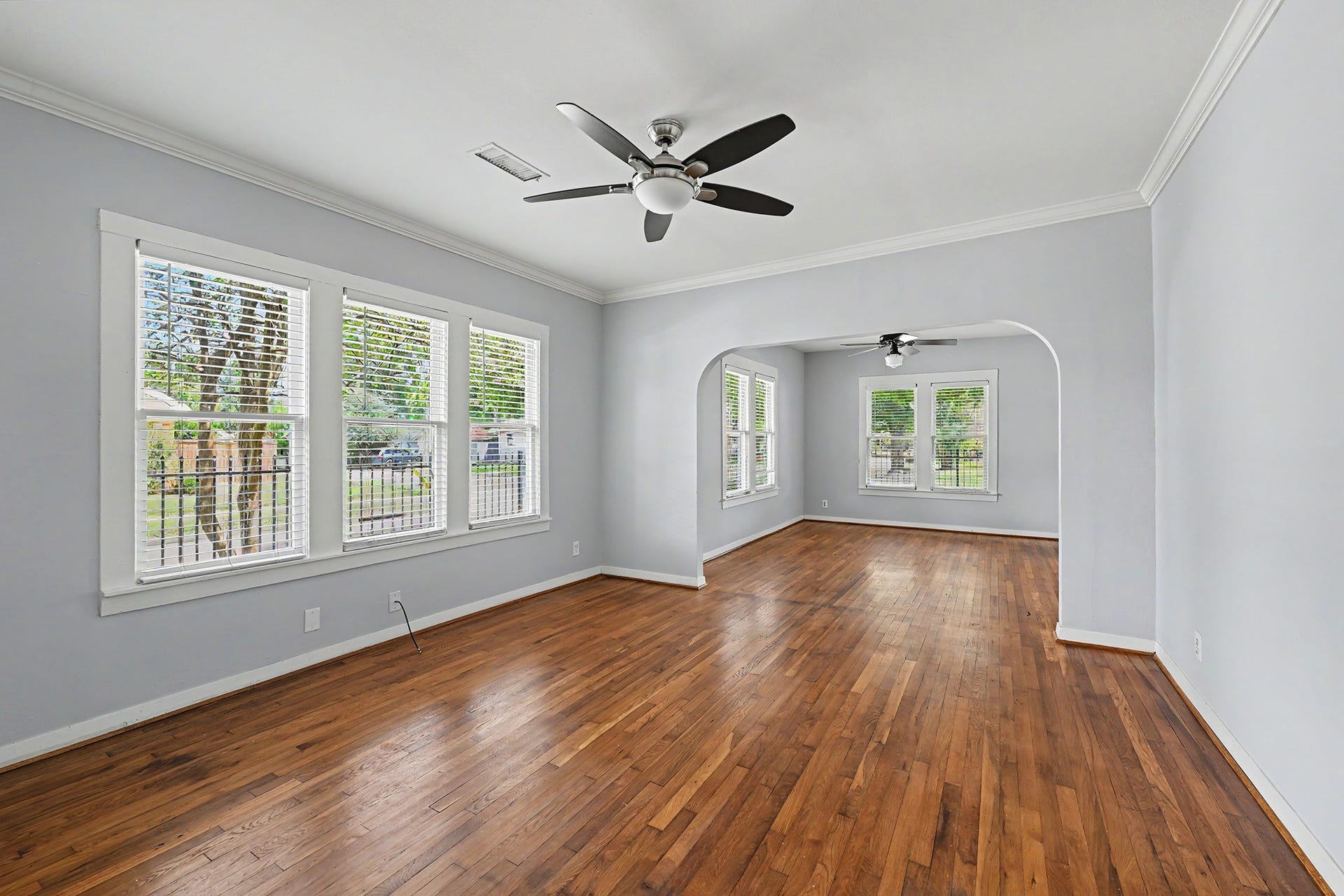 View from the dining room toward the living room highlights crown molding, ceiling fans, and large windows that fill both spaces with natural light.