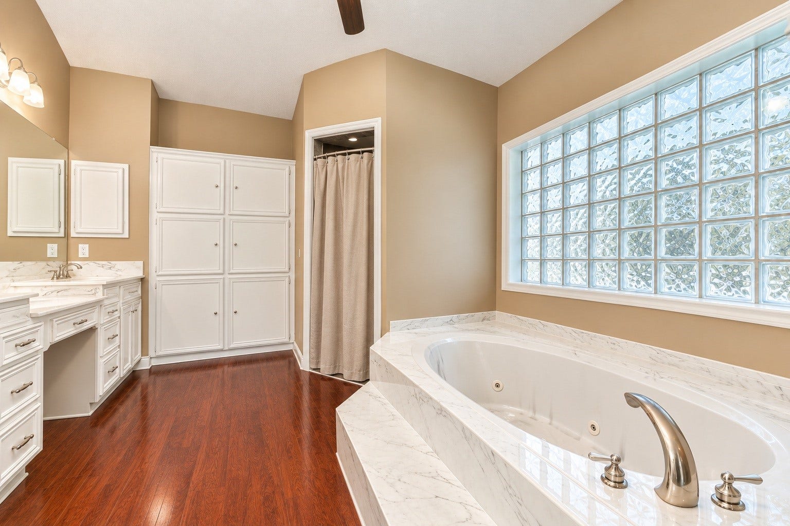 4030 Larkspur Street, Alvin, TX 77511 Luxurious master bathroom featuring a spacious corner jacuzzi tub, elegant glass block window, and dual-sink vanity with ample storage.