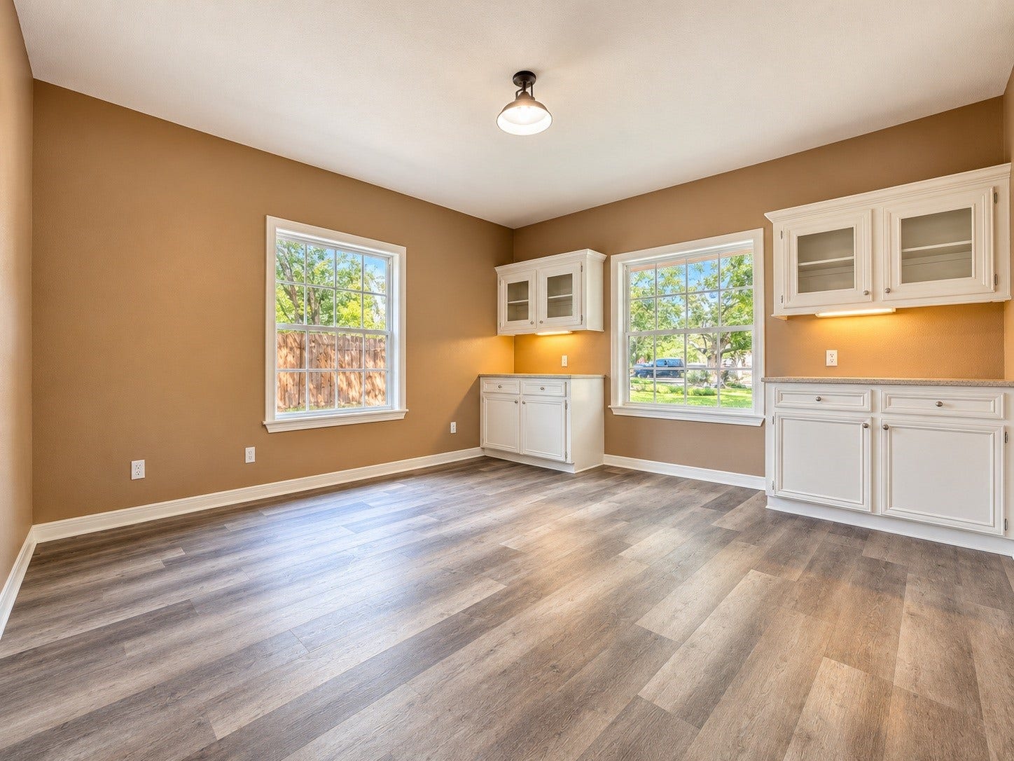 4030 Larkspur Street, Alvin, TX 77511 Bright and inviting dining room with warm-toned walls, featuring large windows for natural light, elegant white cabinetry with glass fronts, and stylish wood-look flooring.