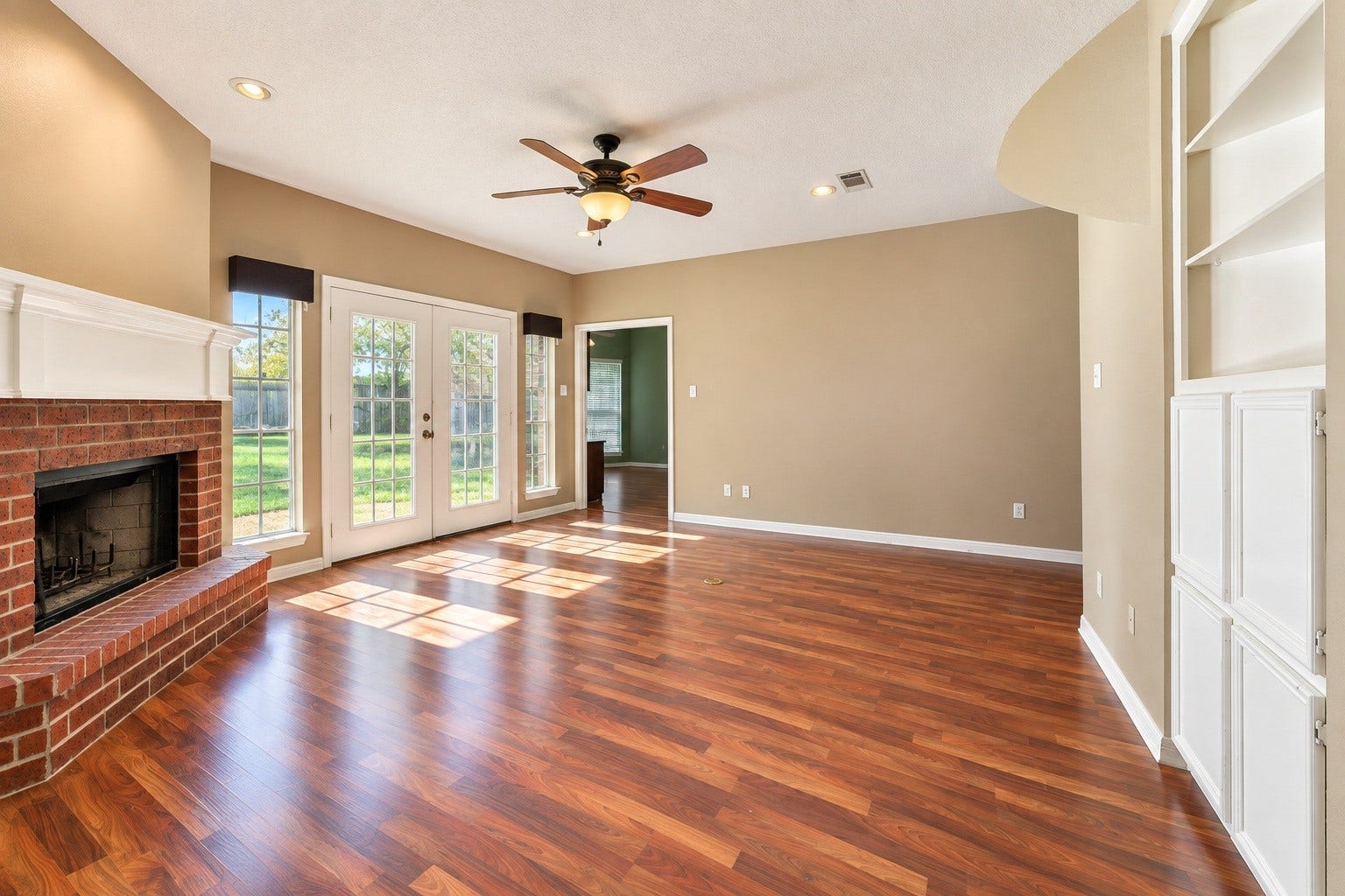 4030 Larkspur Street, Alvin, TX 77511 Inviting living room with rich wood-look floors, a cozy brick fireplace, and abundant natural light streaming through French doors that open to a lush backyard.