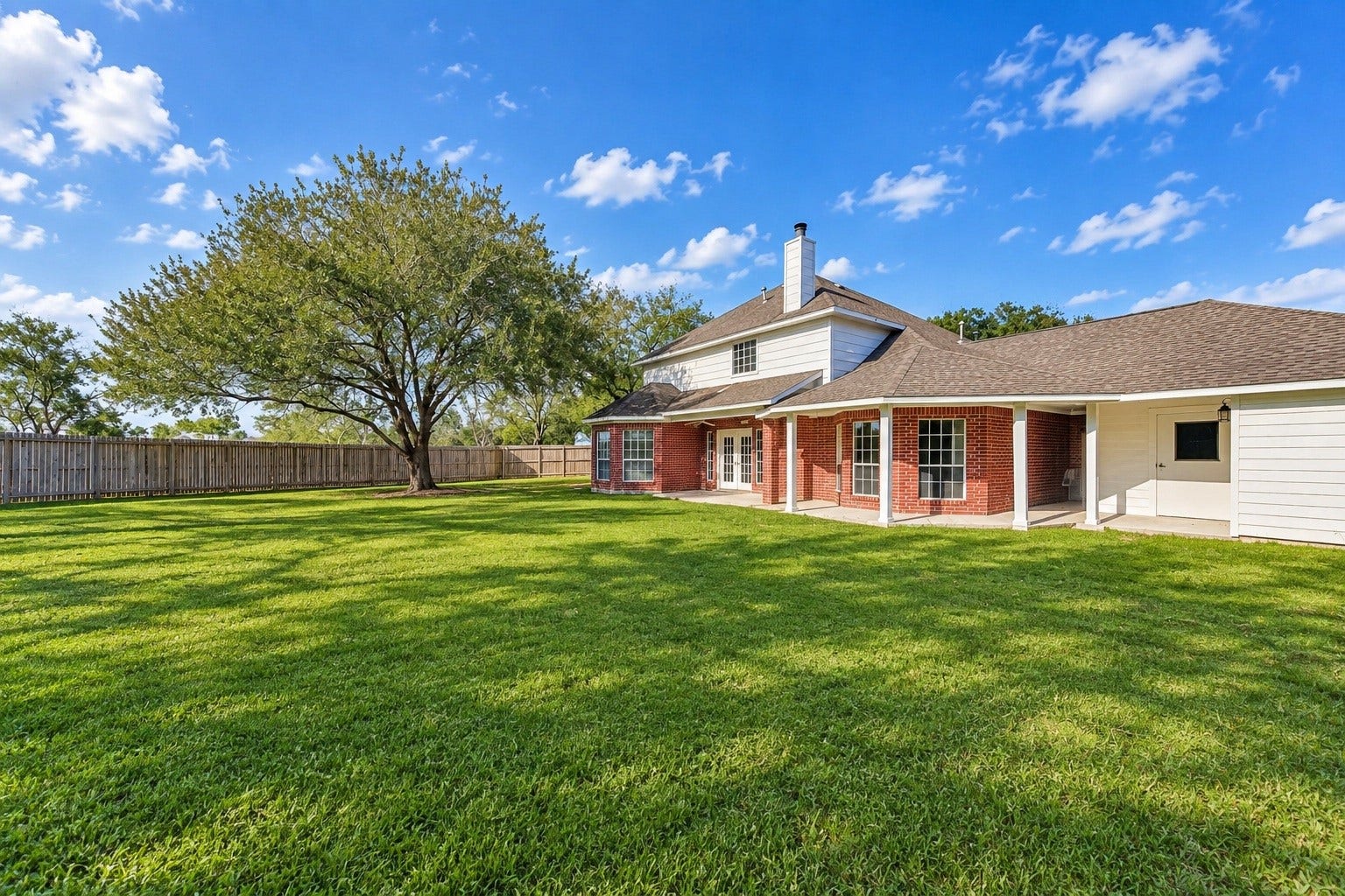 4030 Larkspur Street, Alvin, TX 77511 Expansive backyard with lush green lawn, mature tree, and charming red brick home featuring a spacious covered patio perfect for outdoor gatherings.