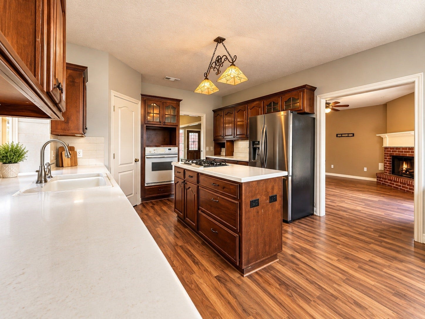 4030 Larkspur Street, Alvin, TX 77511 Spacious kitchen with rich wood cabinetry, modern stainless steel refrigerator, and a central island, seamlessly flowing into a cozy living room with a warm fireplace.
