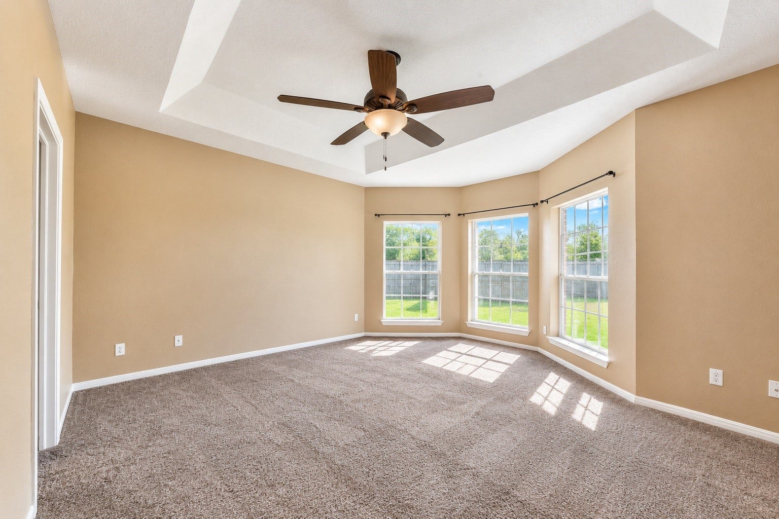 4030 Larkspur Street, Alvin, TX 77511 Spacious master bedroom with a tray ceiling, modern ceiling fan, and large bay windows offering abundant natural light and serene backyard views.
