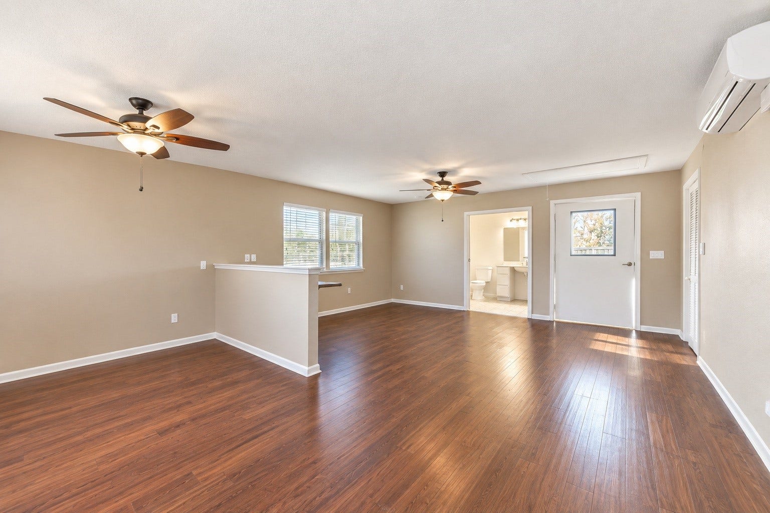 4030 Larkspur Street, Alvin, TX 77511 Spacious detached living area with rich wood-look flooring, neutral walls, and ceiling fans, leading to a bright bathroom and adjacent to a cozy nook with natural light.