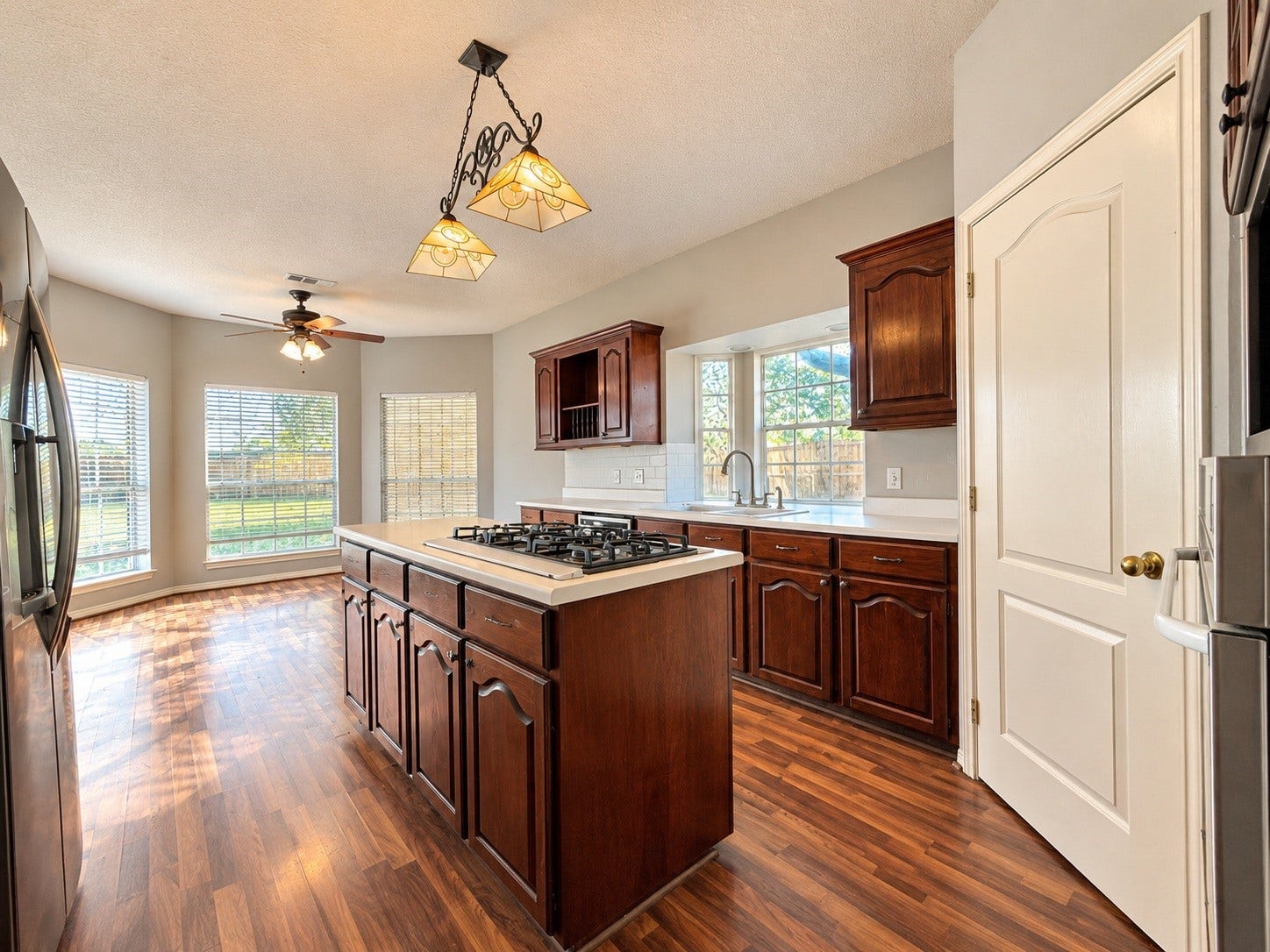 4030 Larkspur Street, Alvin, TX 77511 Spacious kitchen featuring rich wooden cabinetry, a central island with a gas cooktop, and large windows offering abundant natural light and views of the backyard.