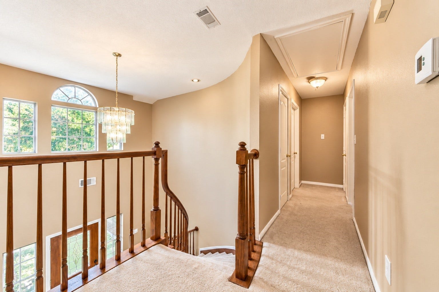 4030 Larkspur Street, Alvin, TX 77511 Bright and inviting upstairs hallway with a charming curved staircase, elegant chandelier, and ample natural light from large windows.