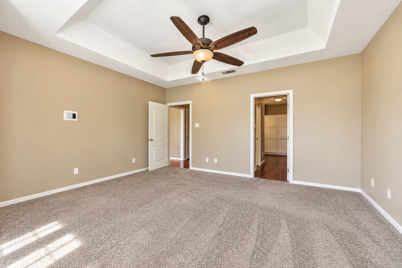 4030 Larkspur Street, Alvin, TX 77511 Spacious master bedroom featuring a tray ceiling, ceiling fan, and plush carpet, with convenient access to the en-suite master bathroom.