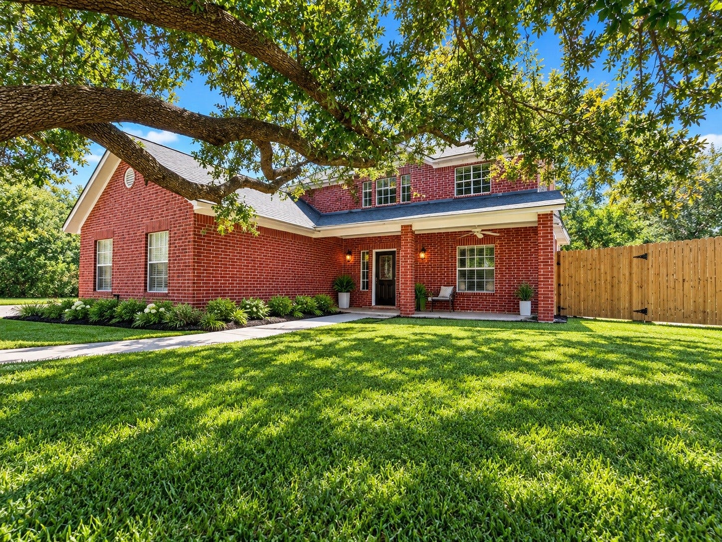 4030 Larkspur Street, Alvin, TX 77511 Charming red brick home with a welcoming front porch, surrounded by lush greenery and mature trees, offering a serene and picturesque setting. Landscaping virtually added for appeal.