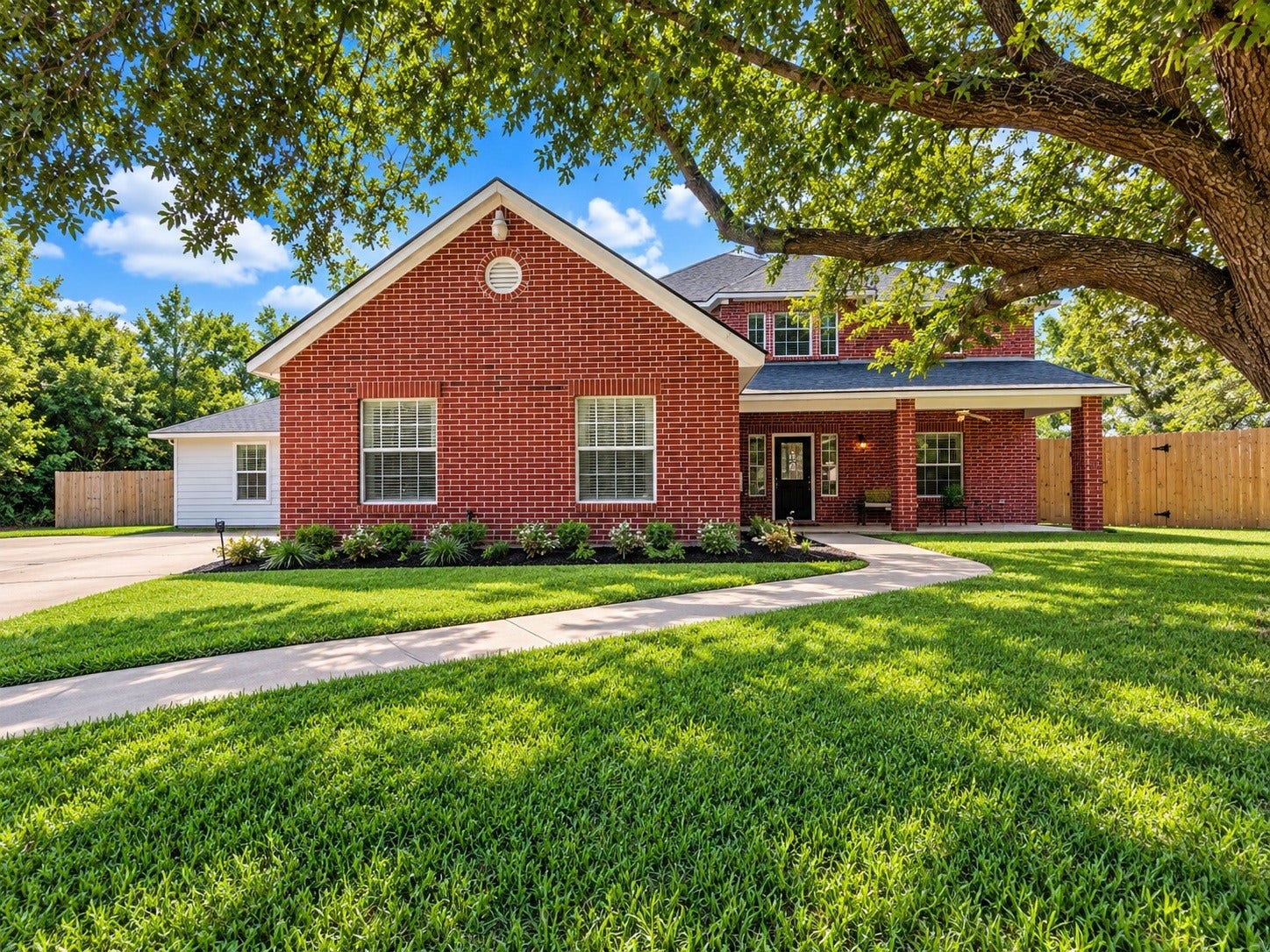 4030 Larkspur Street, Alvin, TX 77511 Charming red brick home with a welcoming front porch, nestled under a mature shade tree, features a well-manicured lawn and a spacious driveway. Landscaping virtually added for appeal.