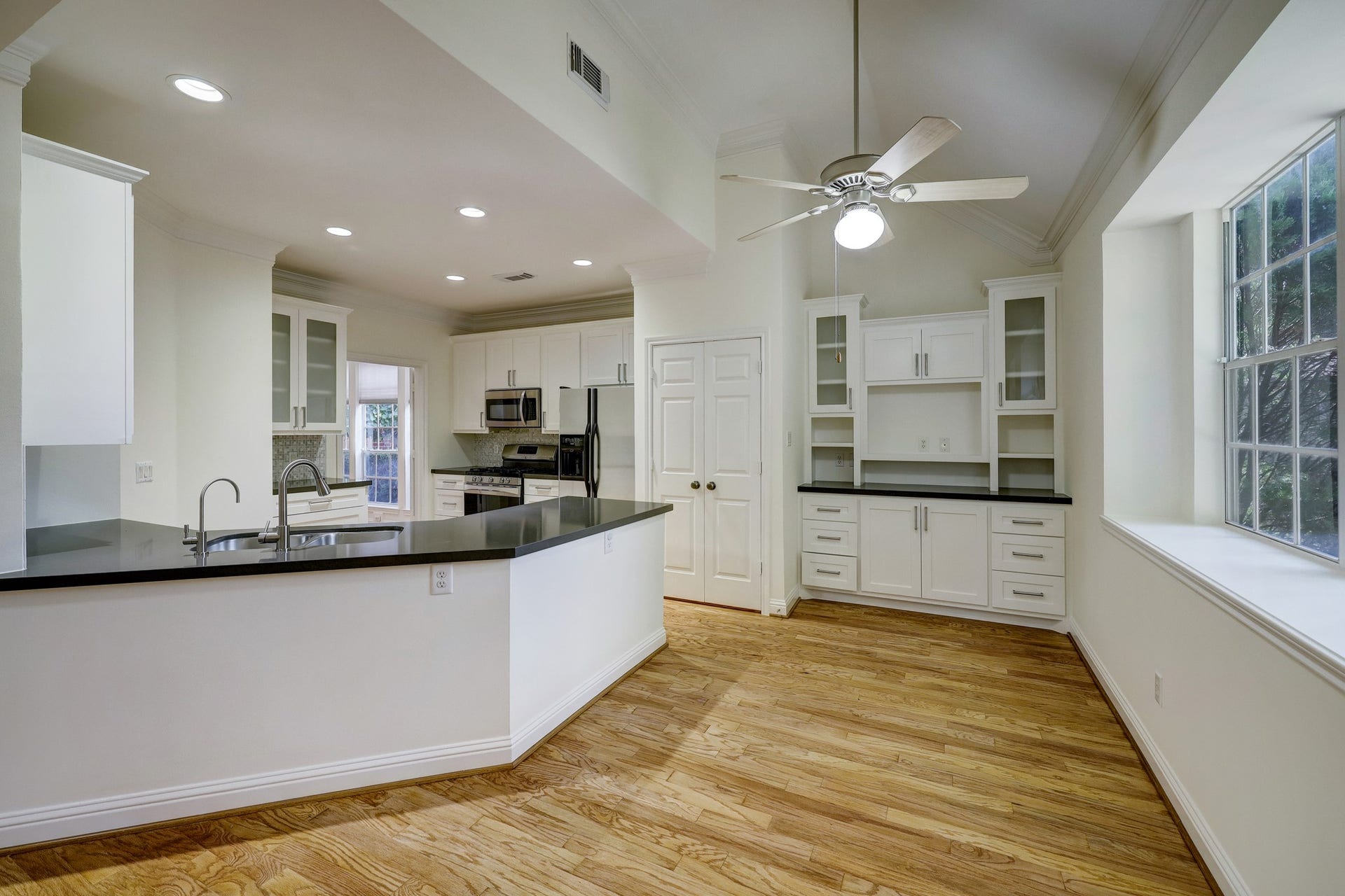 3608 Timberside Circle Drive, Houston, TX 77025 KITCHEN & BREAKFAST ROOM: Bright and functional space featuring new stainless steel dishwasher and refrigerator, white cabinetry with glass-front uppers, sleek black countertops, and a central island with double sink. The breakfast area offers built-in storage and large windows for abundant natural light.