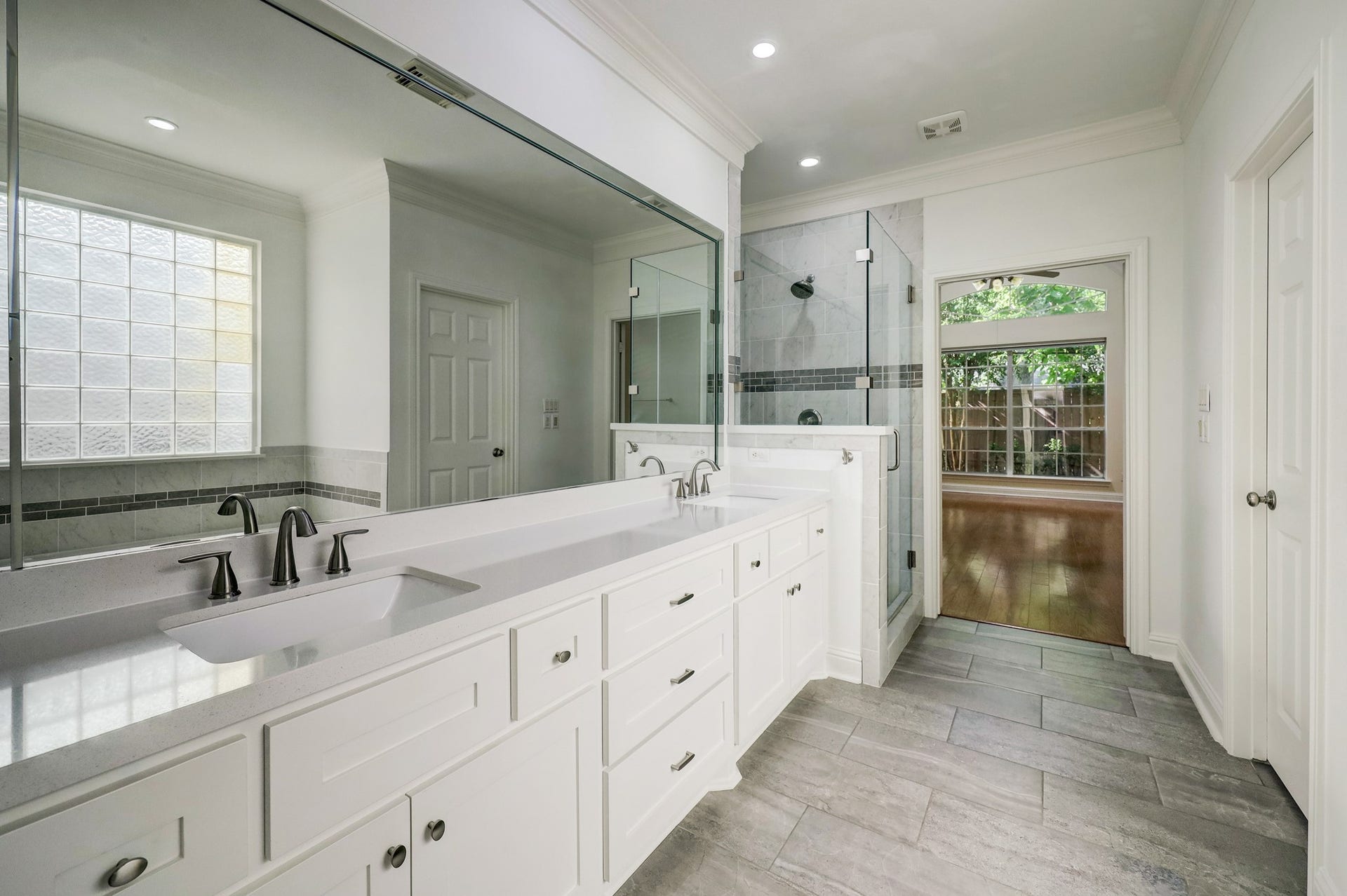 3608 Timberside Circle Drive, Houston, TX 77025 PRIMARY BATHROOM: Elegant and spacious with a double vanity, modern fixtures, and a glass-enclosed shower. Natural light enhances the neutral tones, creating a serene and functional retreat.