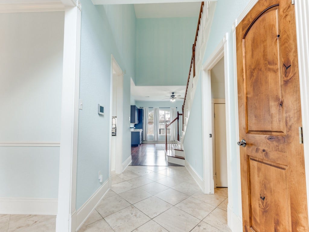 2811 Princeton Street, Houston, TX 77009 This inviting entryway features light blue walls, tiled flooring, and a wooden staircase leading to the second floor. The space opens up to a bright area with large windows and access to the kitchen, showcasing a blend of tile and wooden elements for a warm, welcoming feel.