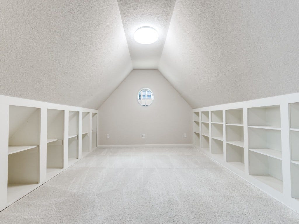 2811 Princeton Street, Houston, TX 77009 This photo showcases the nook off the 2nd bedroom space. A barn door separates it from the main room. It has a sloped ceiling, built-in shelving along both sides for ample storage. The room is well-lit by a circular window at the end and a ceiling light, offering a clean, carpeted floor.