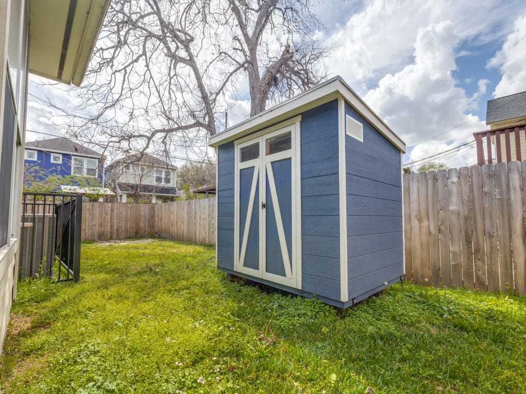 2811 Princeton Street, Houston, TX 77009 This backyard features a small blue storage shed with white trim, set on a grassy area enclosed by a wooden fence, providing a private and functional storage space.