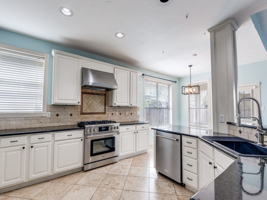 2811 Princeton Street, Houston, TX 77009 Bright and spacious kitchen with modern stainless steel appliances, white cabinetry, and black granite countertops. It features a gas stove, tiled backsplash, and large windows for natural light. The open layout includes a dining area with a stylish pendant light.