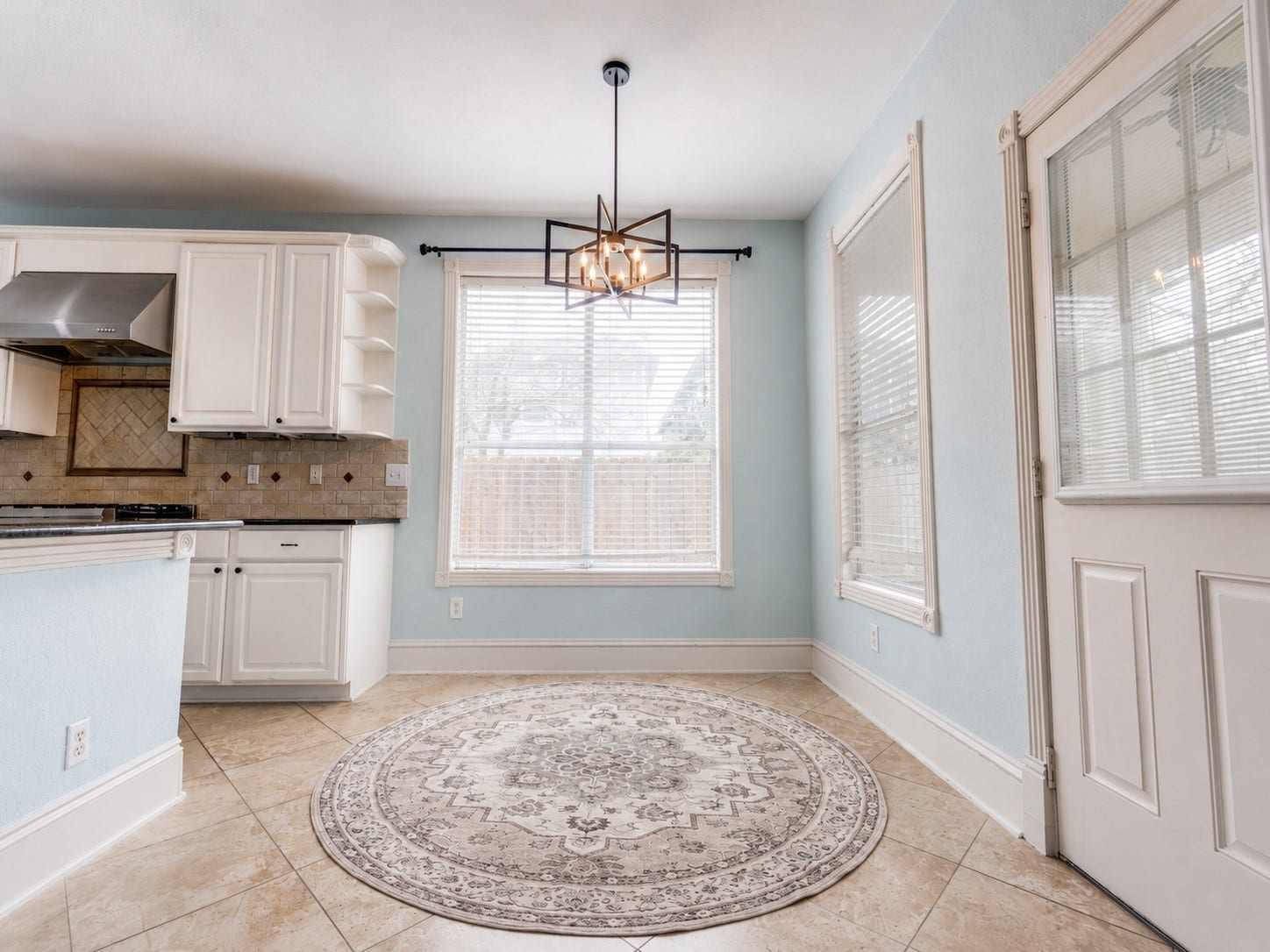 2811 Princeton Street, Houston, TX 77009 Bright kitchen area with large windows, modern light fixture.Features tiled flooring, white cabinets, and a glass-panel door, creating an inviting and airy atmosphere.