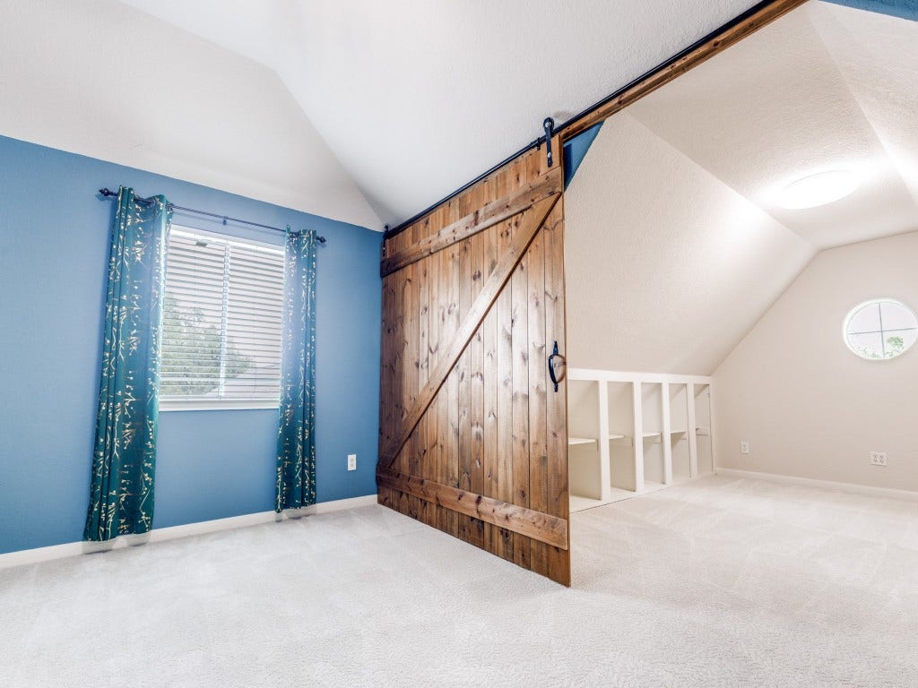 2811 Princeton Street, Houston, TX 77009 This room features a vaulted ceiling, a rustic sliding barn door, and a cozy nook with built-in shelving. The space is brightened by a window with decorative curtains, offering a charming and functional area which might make a perfect workout room or nursery.