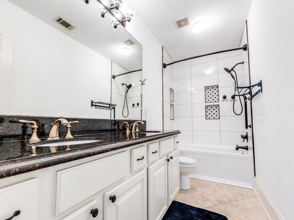 2811 Princeton Street, Houston, TX 77009 This bathroom features a modern design with a spacious double vanity, sleek granite countertops, and elegant fixtures. The shower-tub combination is accented with stylish tile work, and the room is well-lit with contemporary lighting.