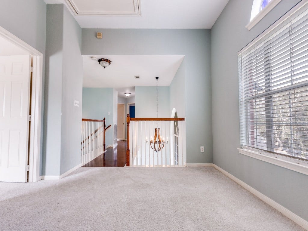 2811 Princeton Street, Houston, TX 77009 Bright and airy upper hallway with carpet flooring, large window with blinds, and a view of the staircase. Features a hanging light fixture and light-colored walls, creating an inviting and open feel.