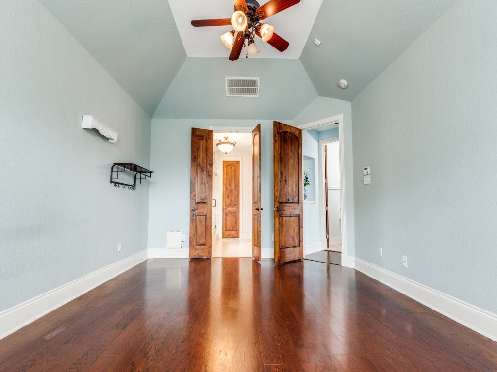 2811 Princeton Street, Houston, TX 77009 Another view of the Primary bedroom which features a vaulted ceiling, rich hardwood floors, and soft blue walls. It has elegant wooden double doors leading to the primary bathroom area.