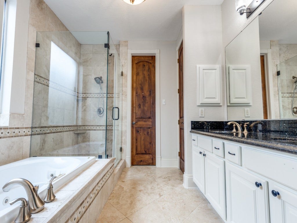 2811 Princeton Street, Houston, TX 77009 The primary bathroom features a luxurious design with a large glass-enclosed shower, a soaking tub, and elegant fixtures. The double vanity has a sleek black countertop, and the room is finished with neutral-toned tiles and a wooden door, creating a sophisticated and inviting space.