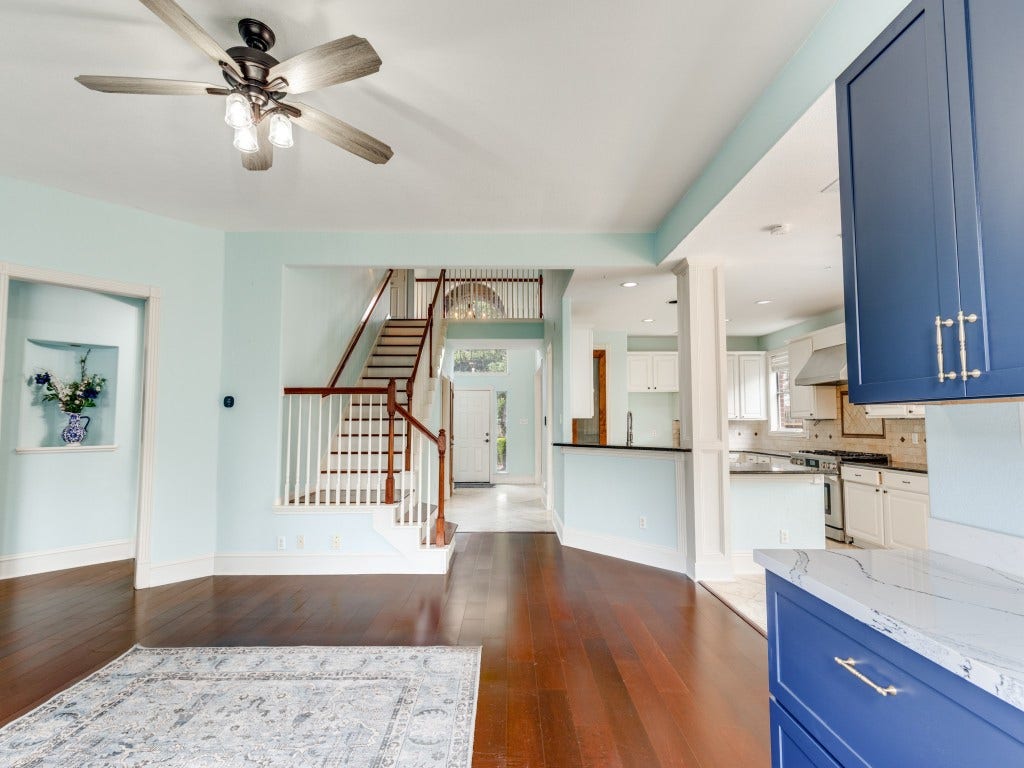 2811 Princeton Street, Houston, TX 77009 This photo showcases a bright, open living area with hardwood floors. The space includes a modern bar with built in wine fridge, blue cabinets and a marble countertop, adjacent to a staircase leading to the upper level, providing a spacious and inviting atmosphere.