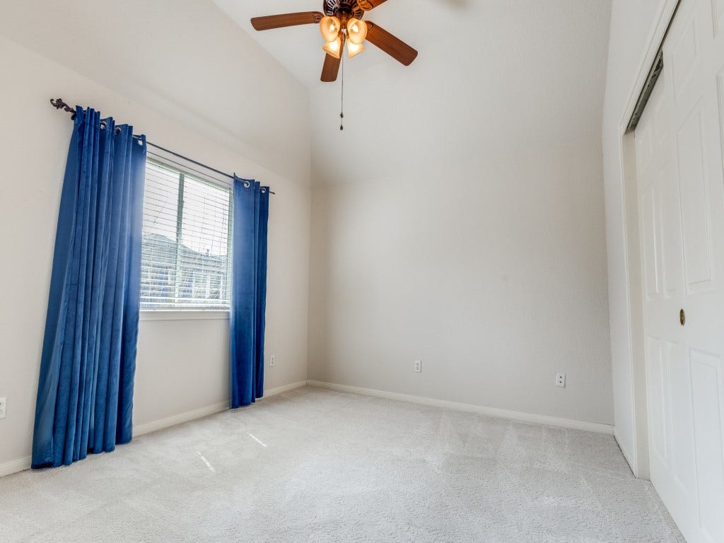 2811 Princeton Street, Houston, TX 77009 Second floor bedroom with vaulted ceiling, ceiling fan, and large window adorned with blue curtains. Features plush carpeting and a sliding door closet.