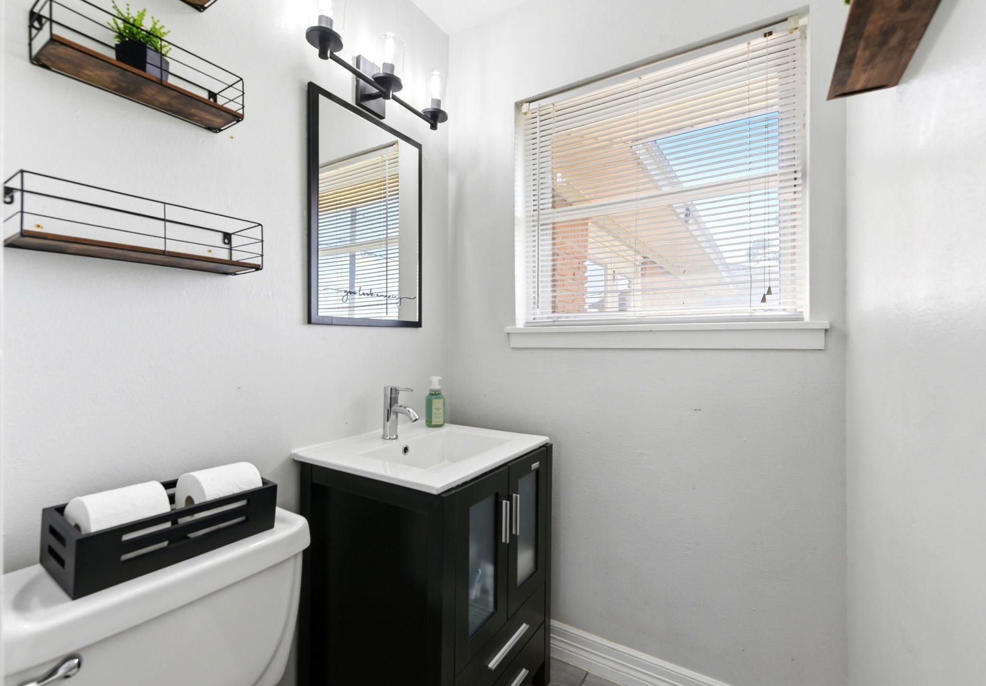 2405 Hillshire Drive, Deer Park, TX 77536 Chic and modern bathroom featuring a sleek black vanity, stylish wall shelves, and ample natural light through a large window.