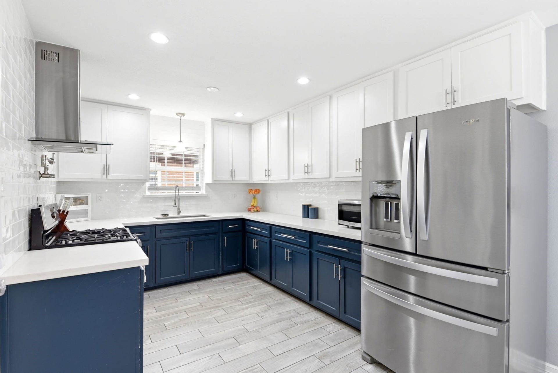 2405 Hillshire Drive, Deer Park, TX 77536 Modern kitchen with sleek stainless steel appliances, elegant two-tone cabinetry in navy and white, and a bright, inviting atmosphere enhanced by recessed lighting and a window over the sink.
