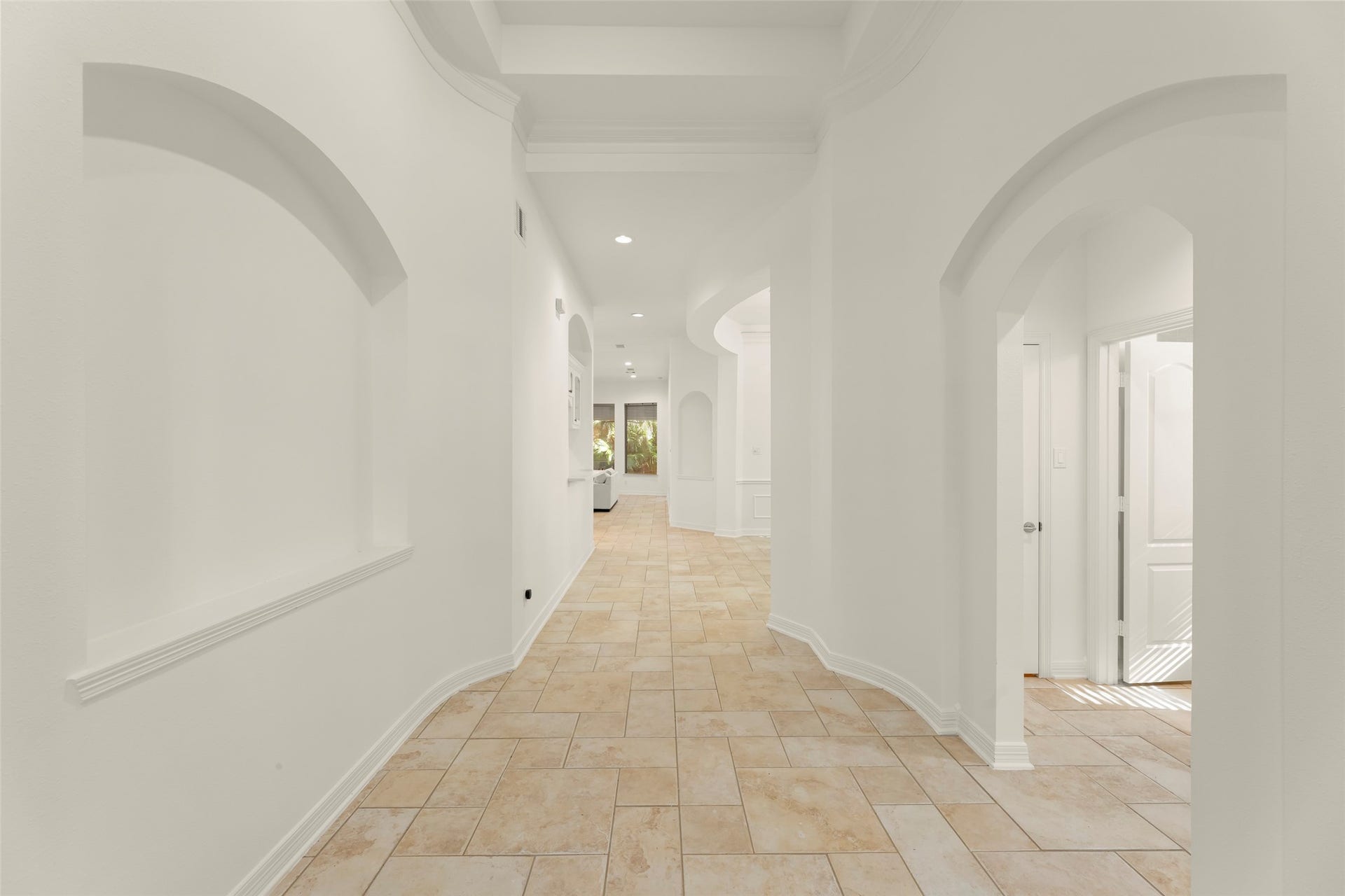 1211 Sterling Court, Katy, TX 77494 Elegant hallway with arched doorways, recessed wall niches, and warm tile flooring, leading to bright living spaces.